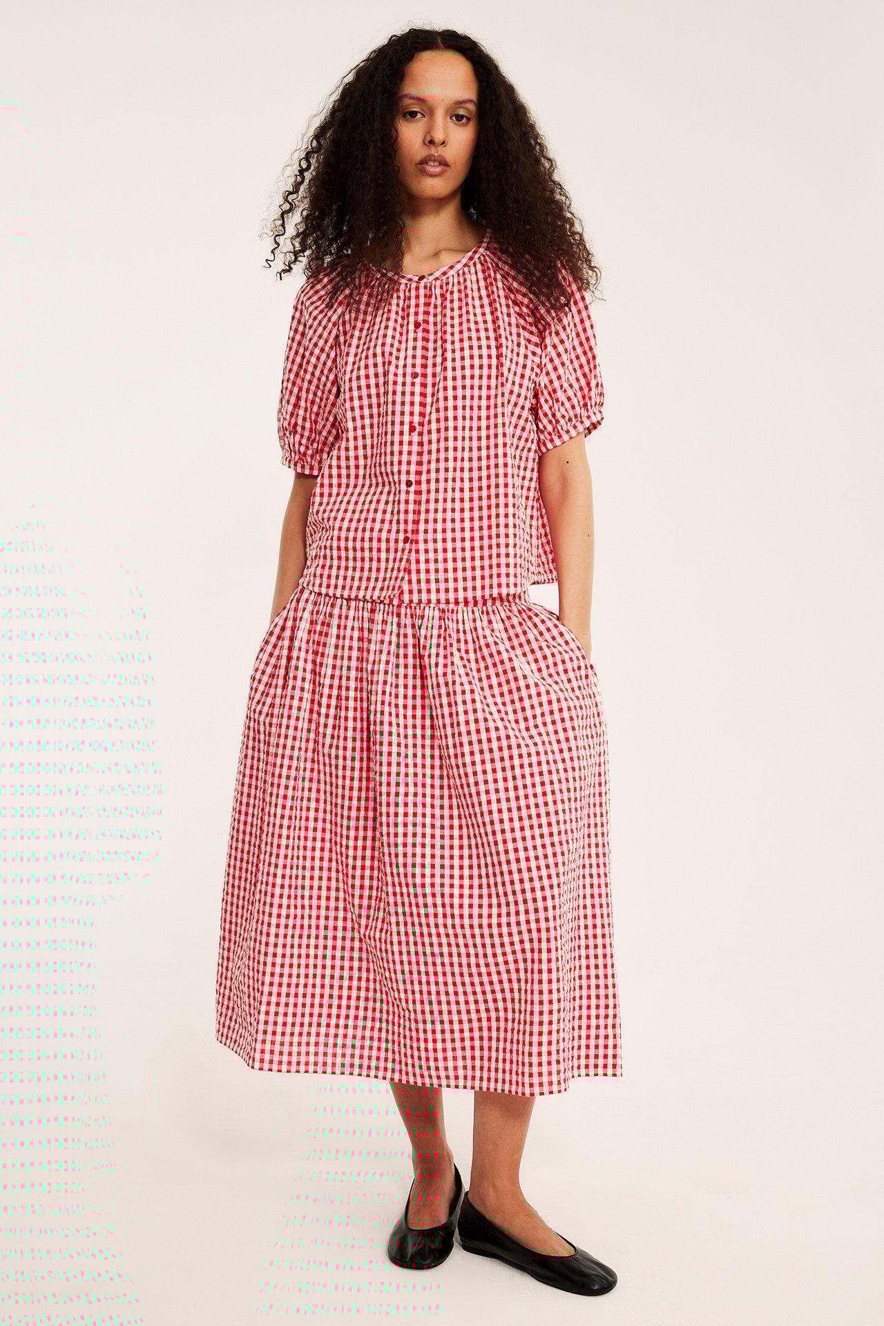 Framsida: Kvinna i rödvit rutig bäckeböljablus, matchande midikjol och svarta skor.
