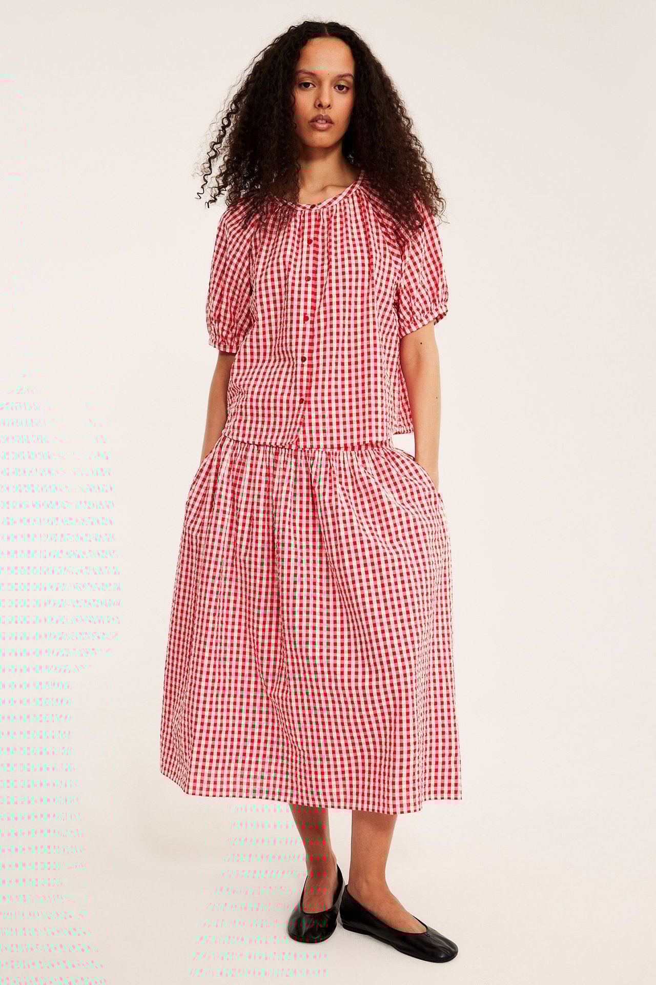 Framsida: Kvinna i rödvit rutig bäckeböljablus, matchande midikjol och svarta skor.