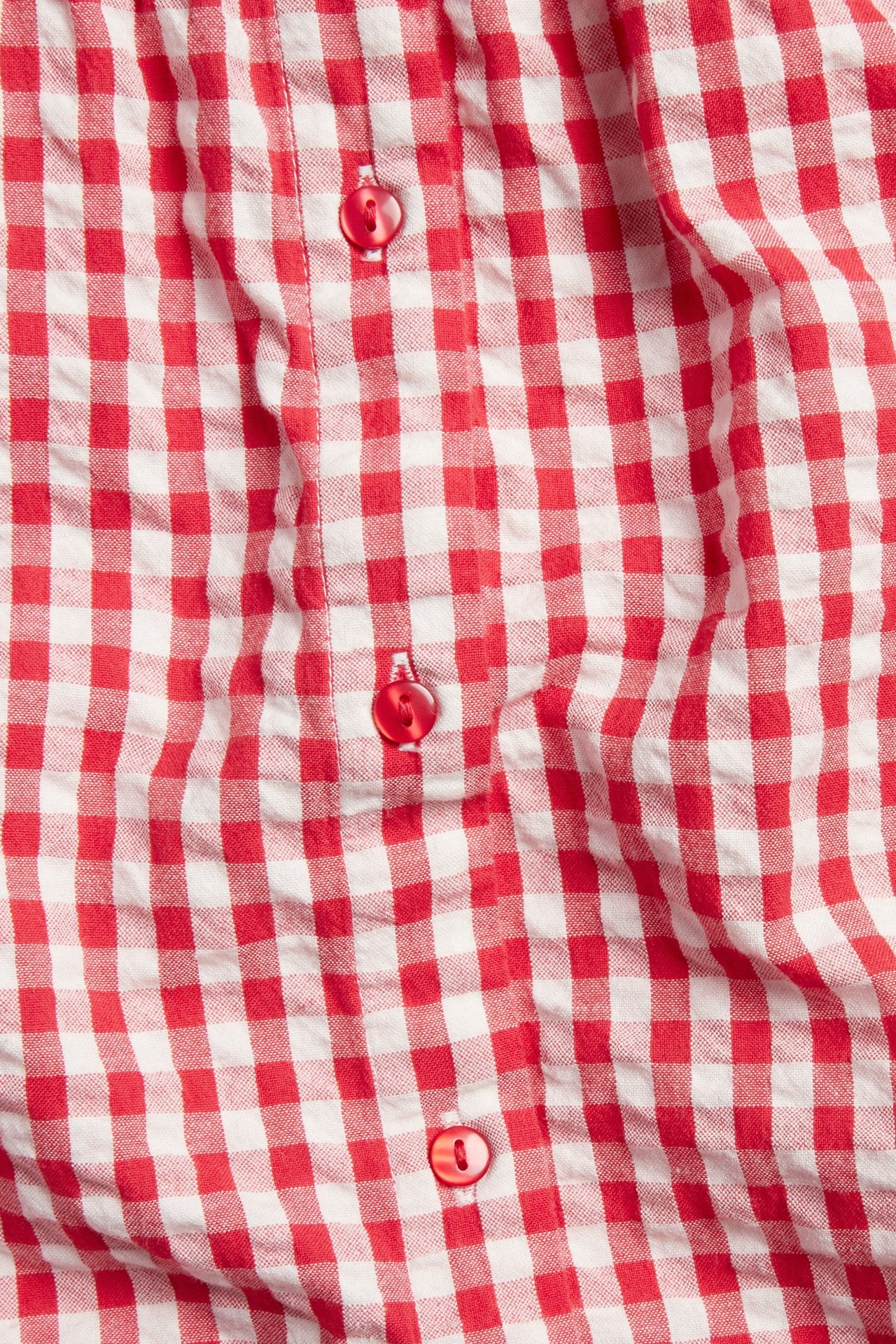 Zbliżenie na czerwono-białą bluzkę bawełnianą z bąbelkowej bawełny w kratę z czerwonymi guzikami.