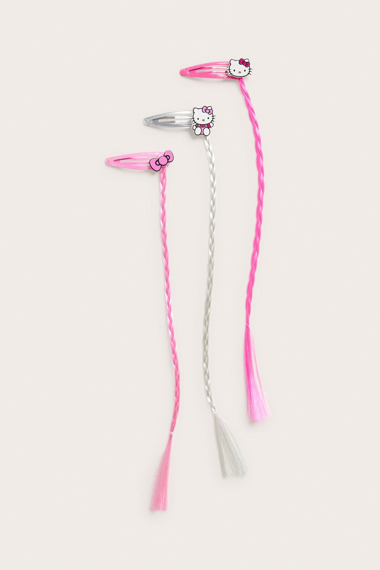 Widok z przodu: Trzy spinki do włosów Hello Kitty z warkoczami; dwie jasnoróżowe, jedna srebrna.