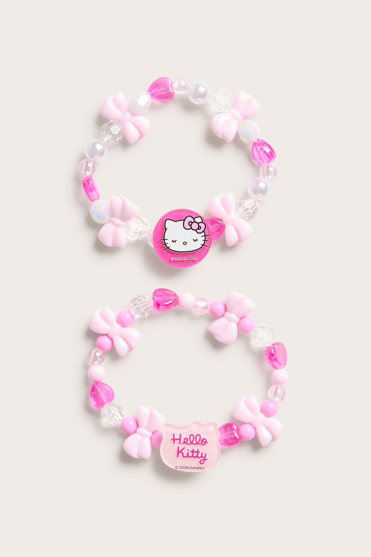 Dwie jasnoróżowe bransoletki z koralików Hello Kitty z zawieszkami i różowymi koralikami, widok z góry.