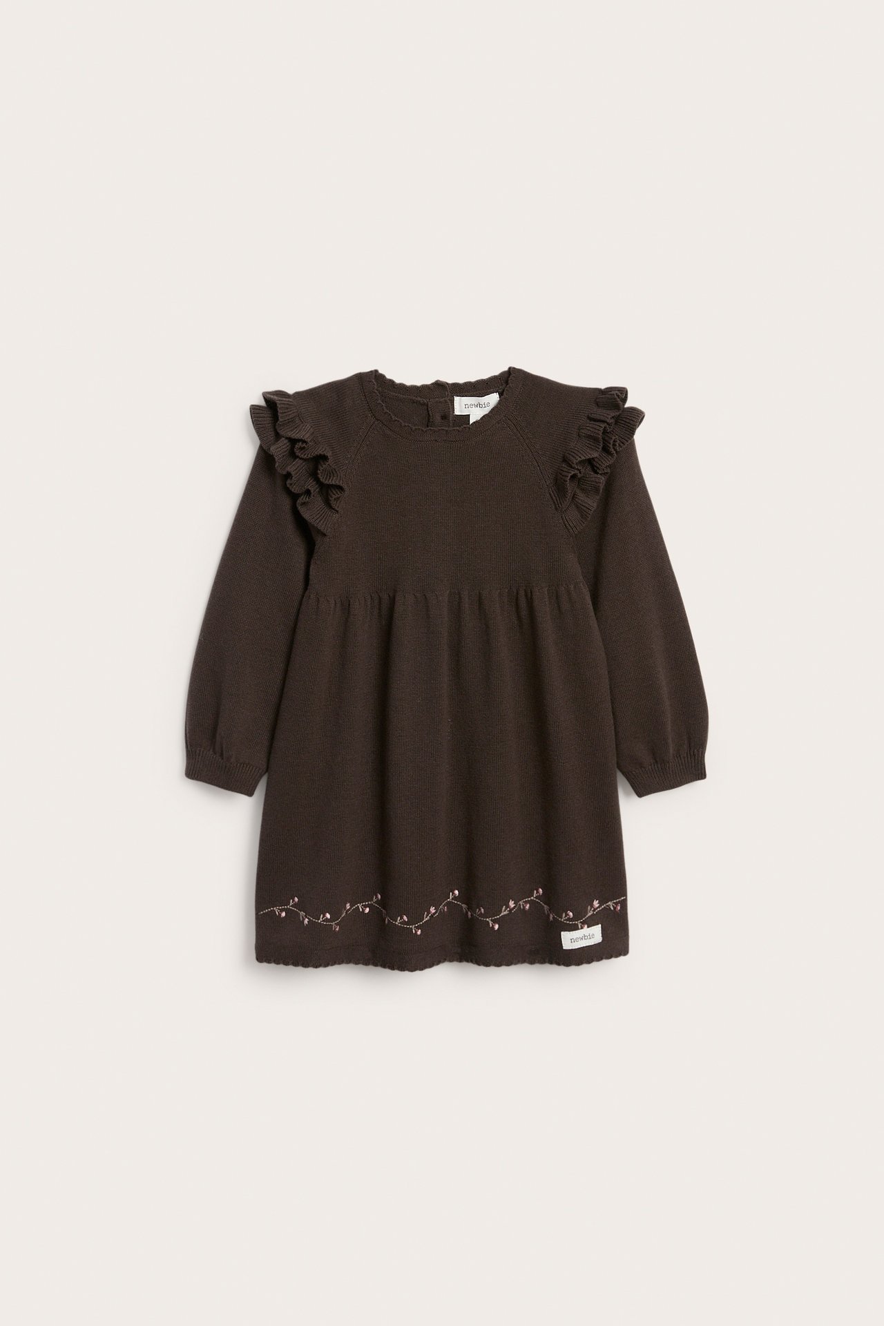 Framifrån, mörkbrun stickad babydress med volangaxlar och blomsterbroderi.