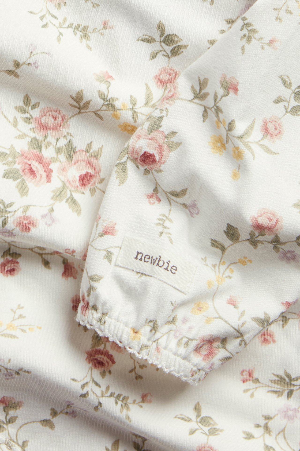 Närbild: offwhite babybody med lång ärm, rosa blommigt mönster, elastiska picotmuddar.