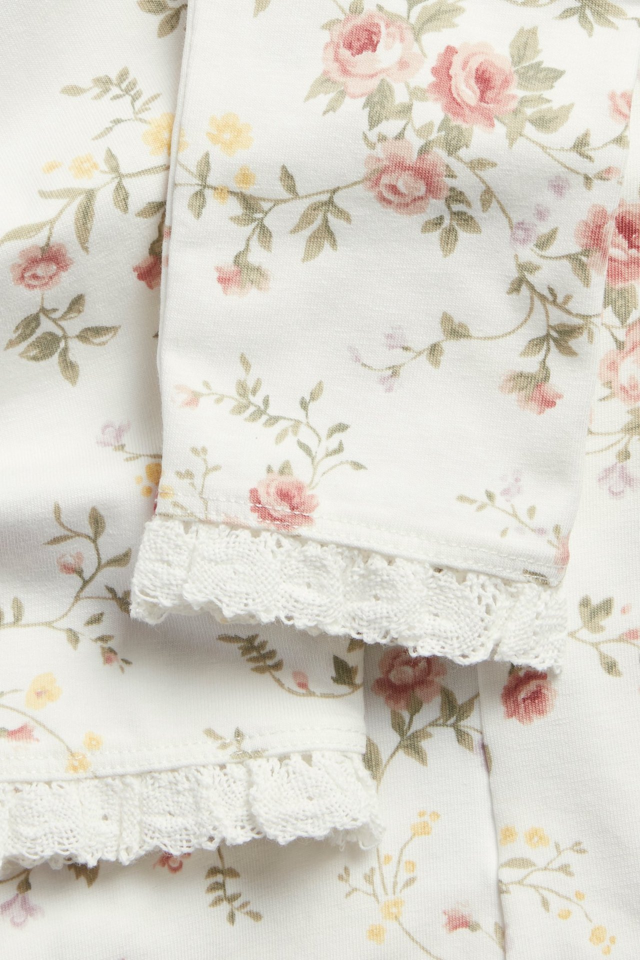 Lähikuva luonnonvalkoisista kukkakuvioisista leggingseistä, joissa on pitsirypytys lahkeensuussa.