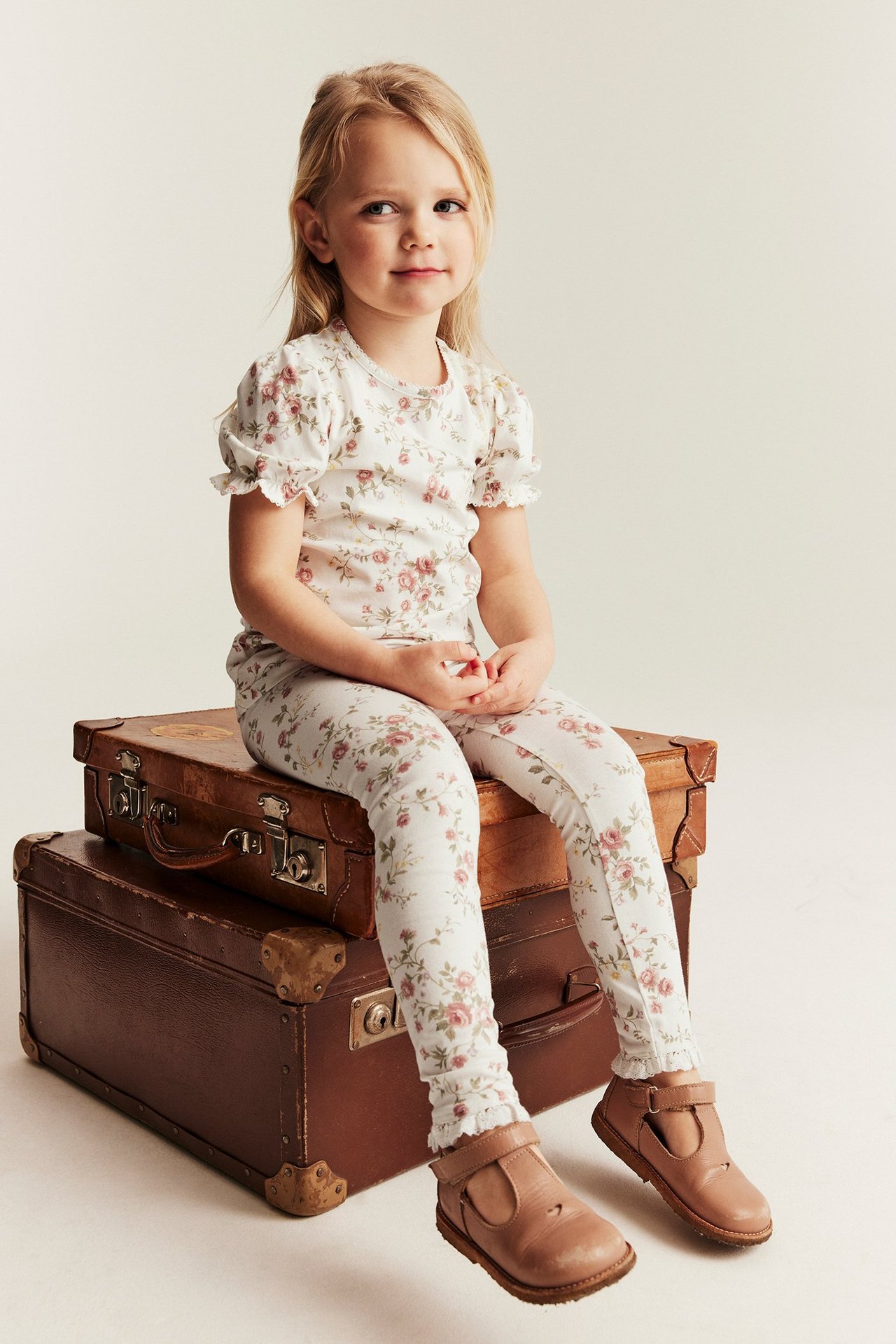 Forfra: Barn bruker offwhite blomstrete leggings med volang, matchende topp og brune T-remssko.