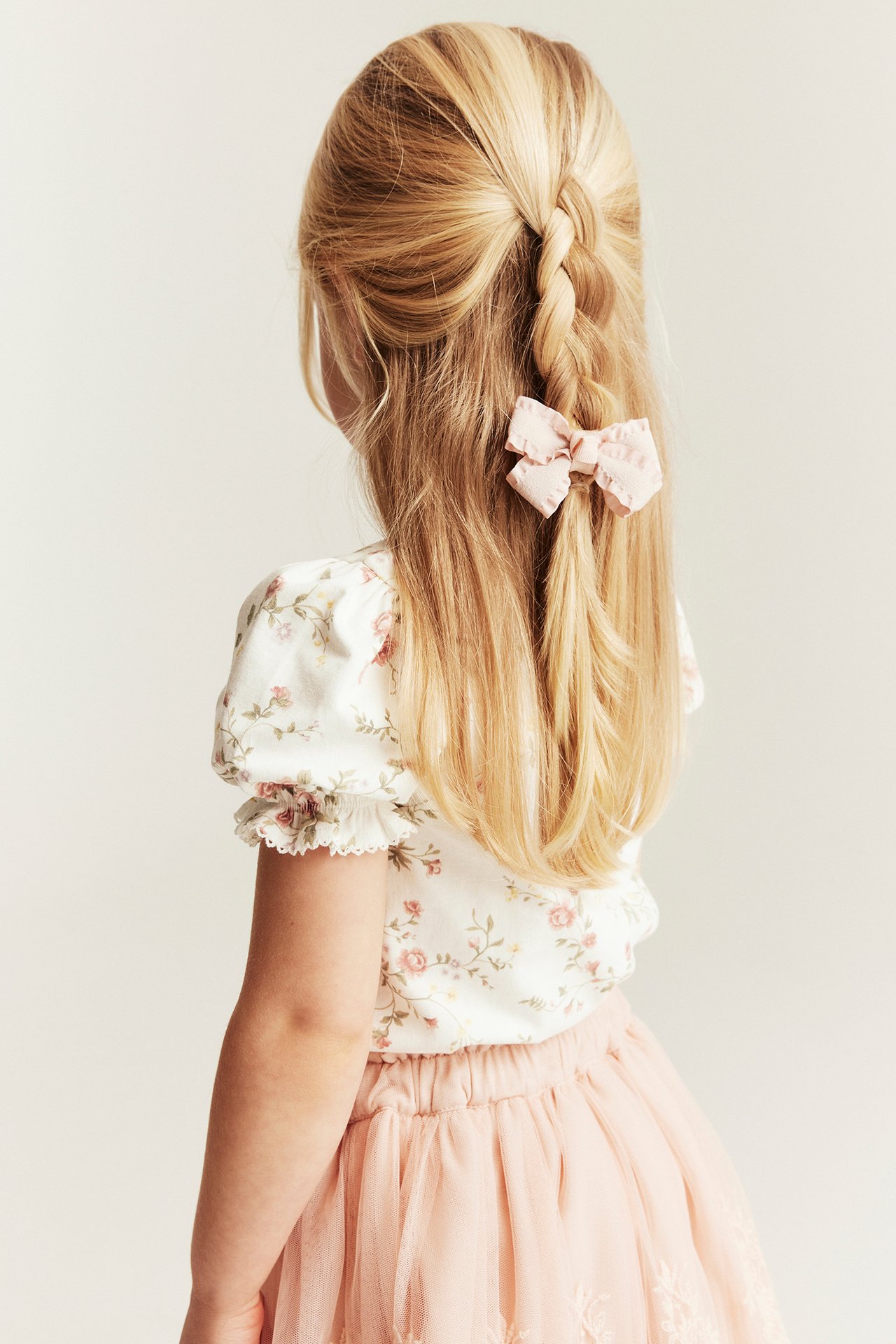 Bakfra: Barn i offwhite blomstrete jerseytopp med puffermer, rosa tyllskjørt og rosa hårsløyfe.