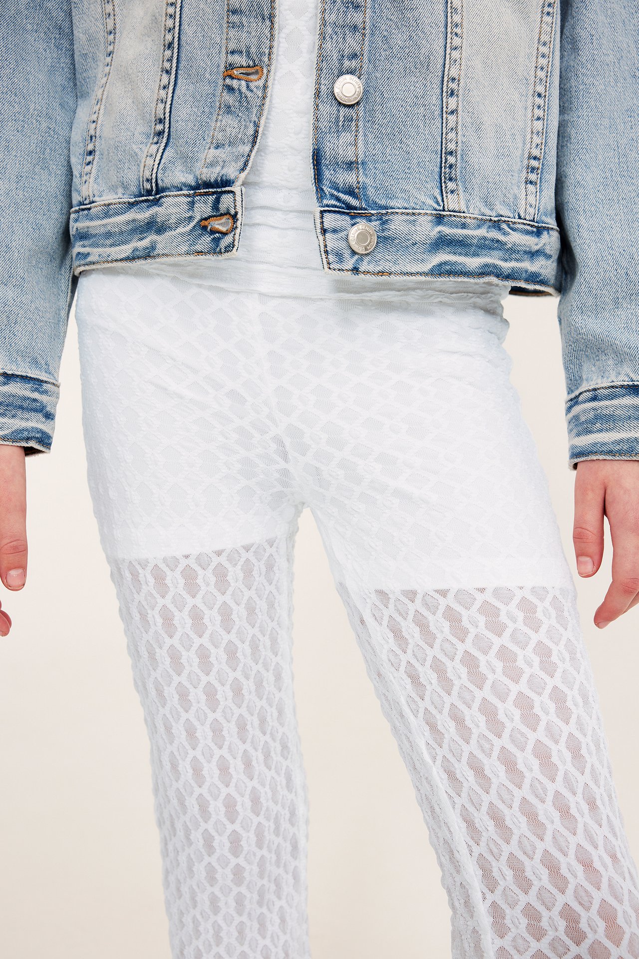 Frontvy av ett barn i vita yogabyxor med spetsmönster och nedvikbar midja, med en jeansjacka.