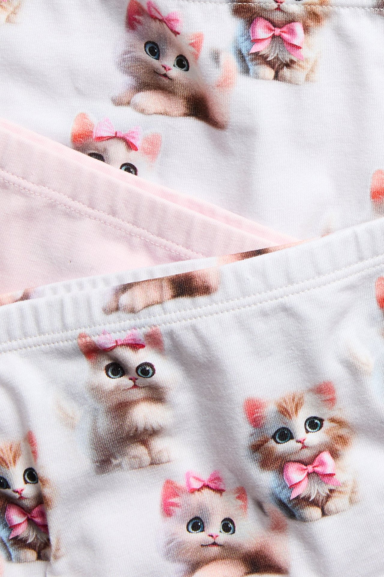 Närbild på tre par barnboxertrosor: två offwhite med kattprint och en enfärgad ljusrosa.