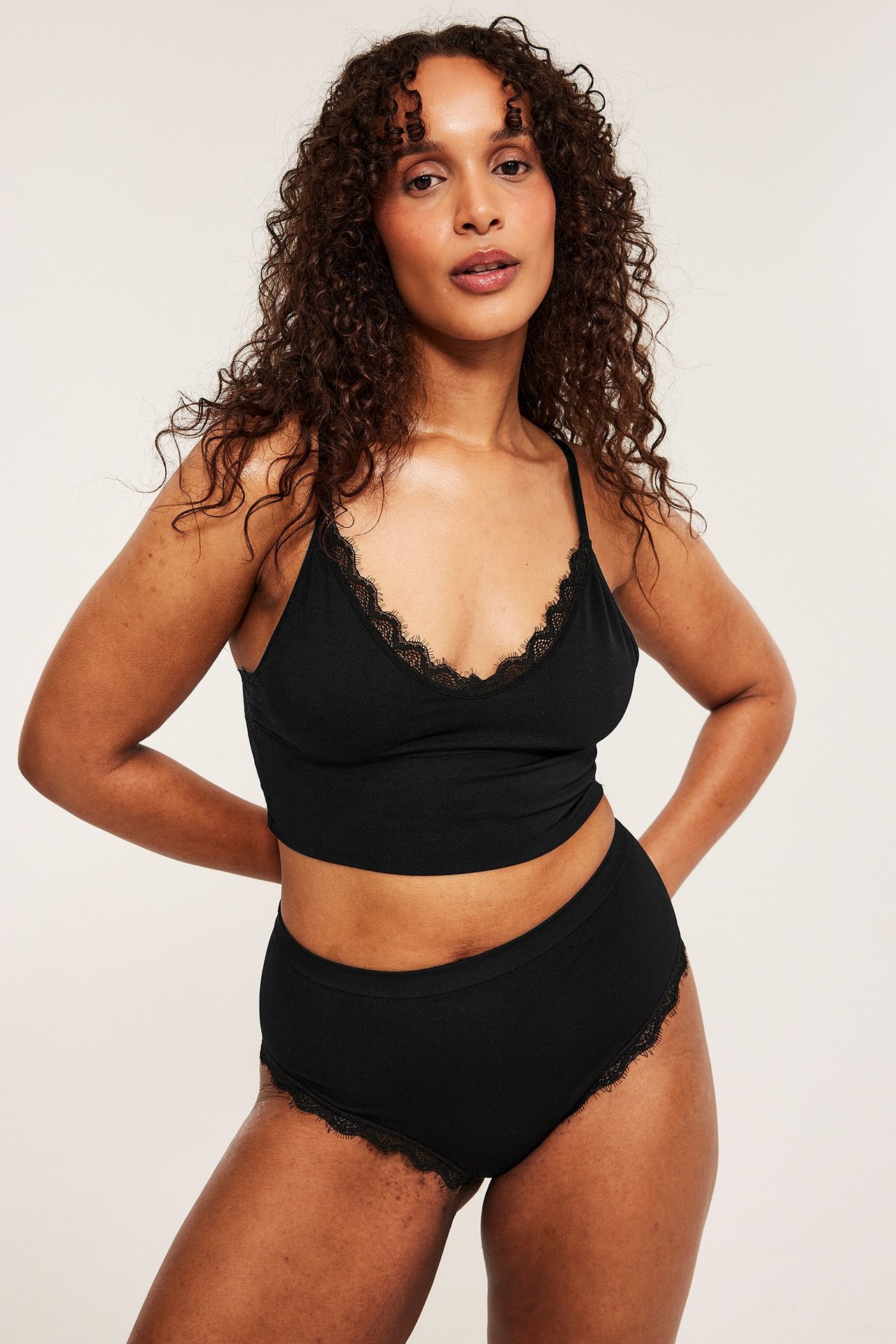 Frontbilde av kvinne i svarte cheeky truser med blonder og matchende svart blonde-bralette.