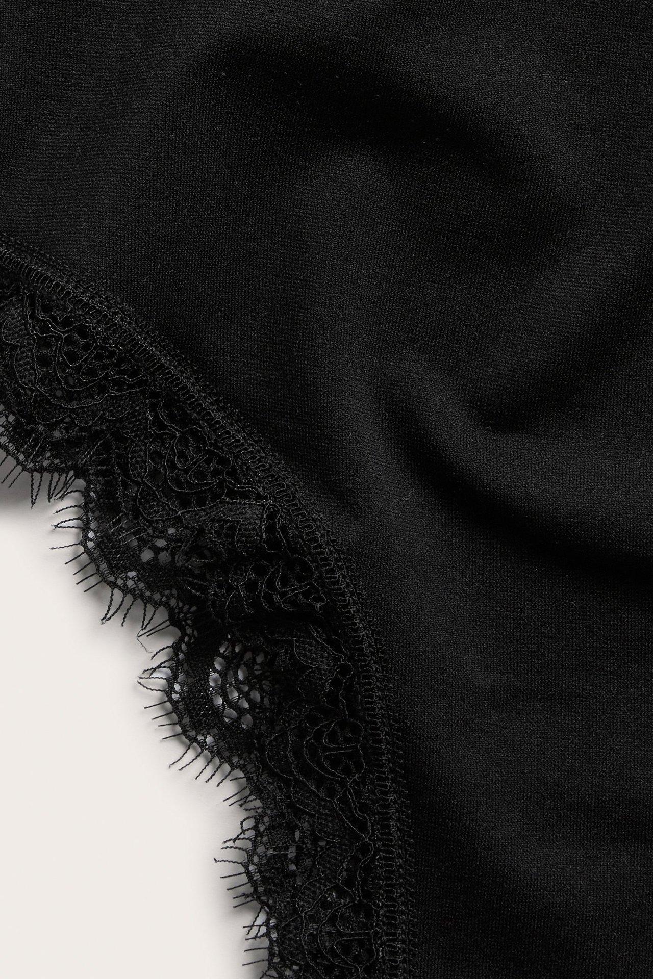 Zbliżenie na jednolite czarne stringi cheeky z delikatnym czarnym koronkowym wykończeniem.