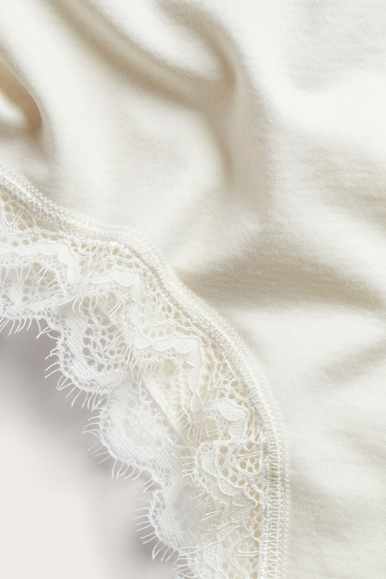 Zbliżenie na off-white figi cheeky z misterną białą koronką na krawędzi.