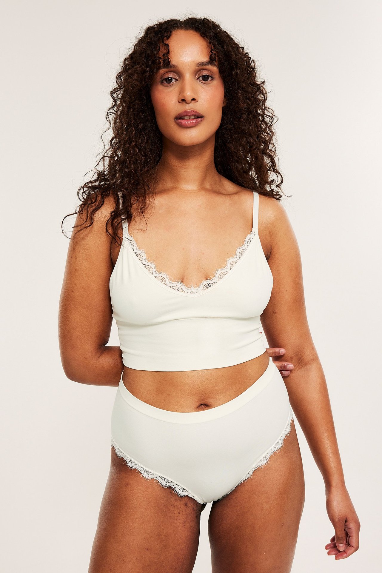 Frontvy av en kvinna som bär offwhite cheeky trosor med spetsdetaljer och en matchande bralette.