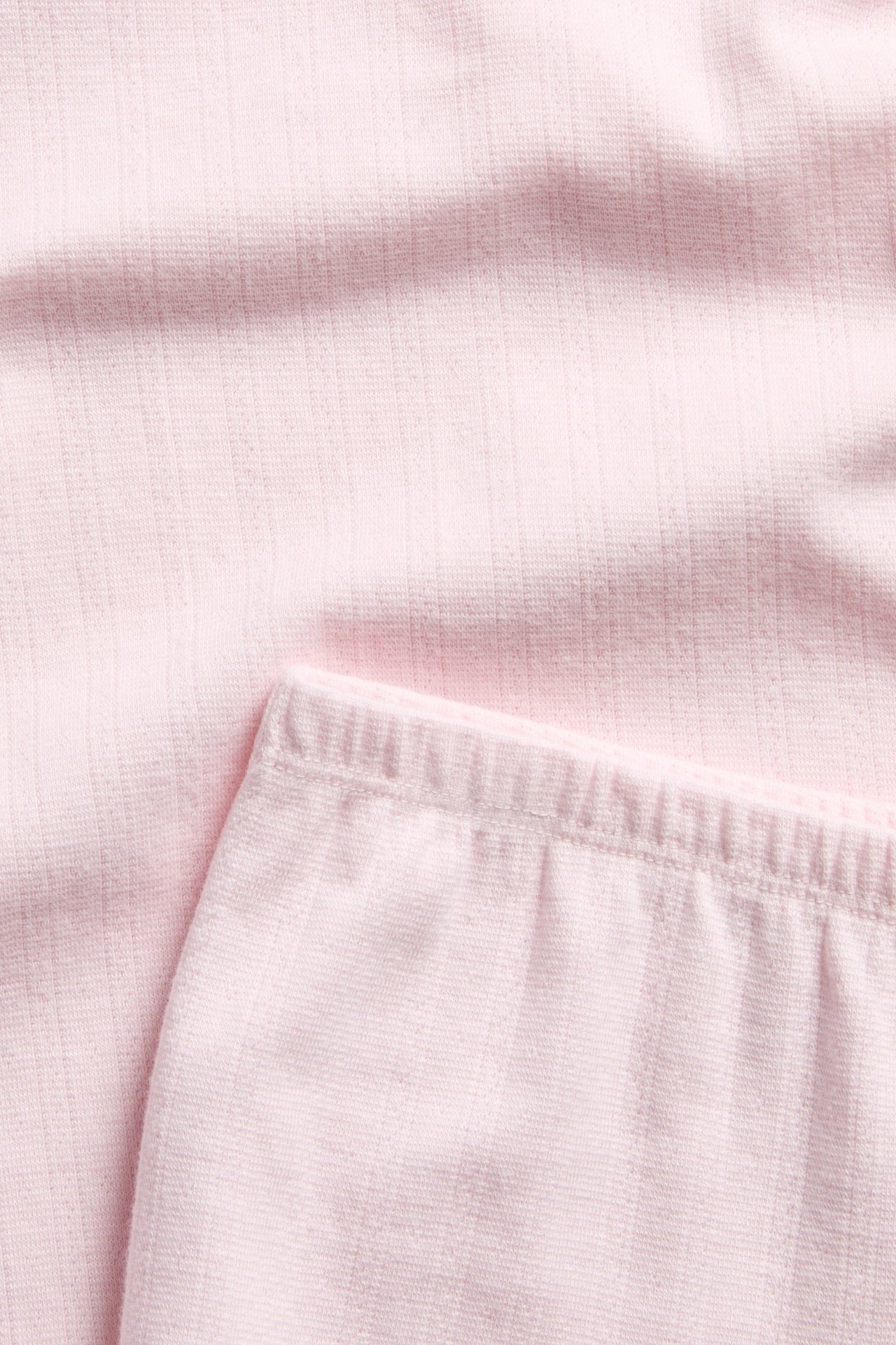 Lähikuva vaaleanpunaisesta pointelle-puuvillapyjamasetistä, jossa lyhythihainen paita ja joustovyötäröiset shortsit.