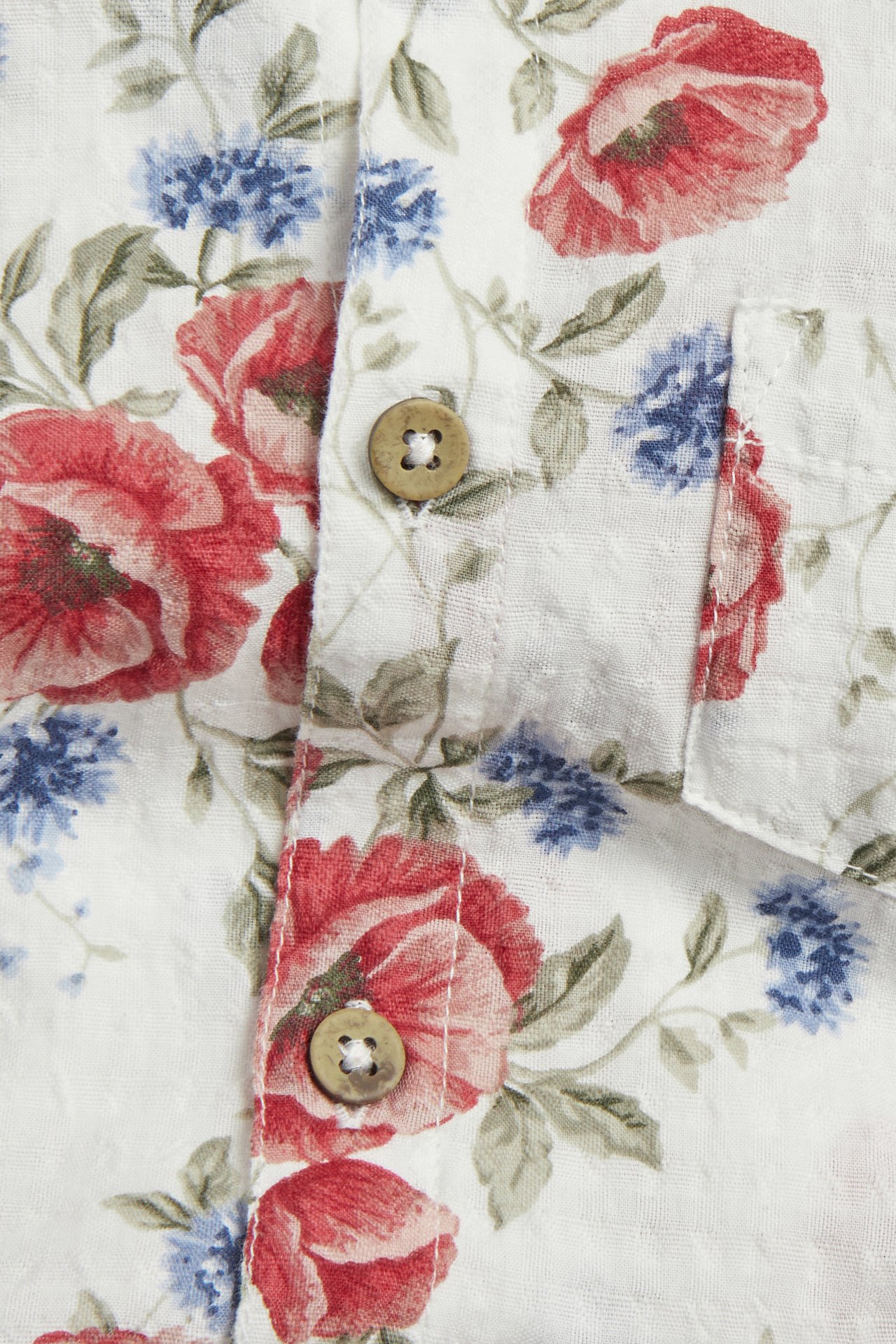 Nærbilde: Offwhite bomullsskjortebody med blomstermønster rød/blå, brune knapper, brystlomme.
