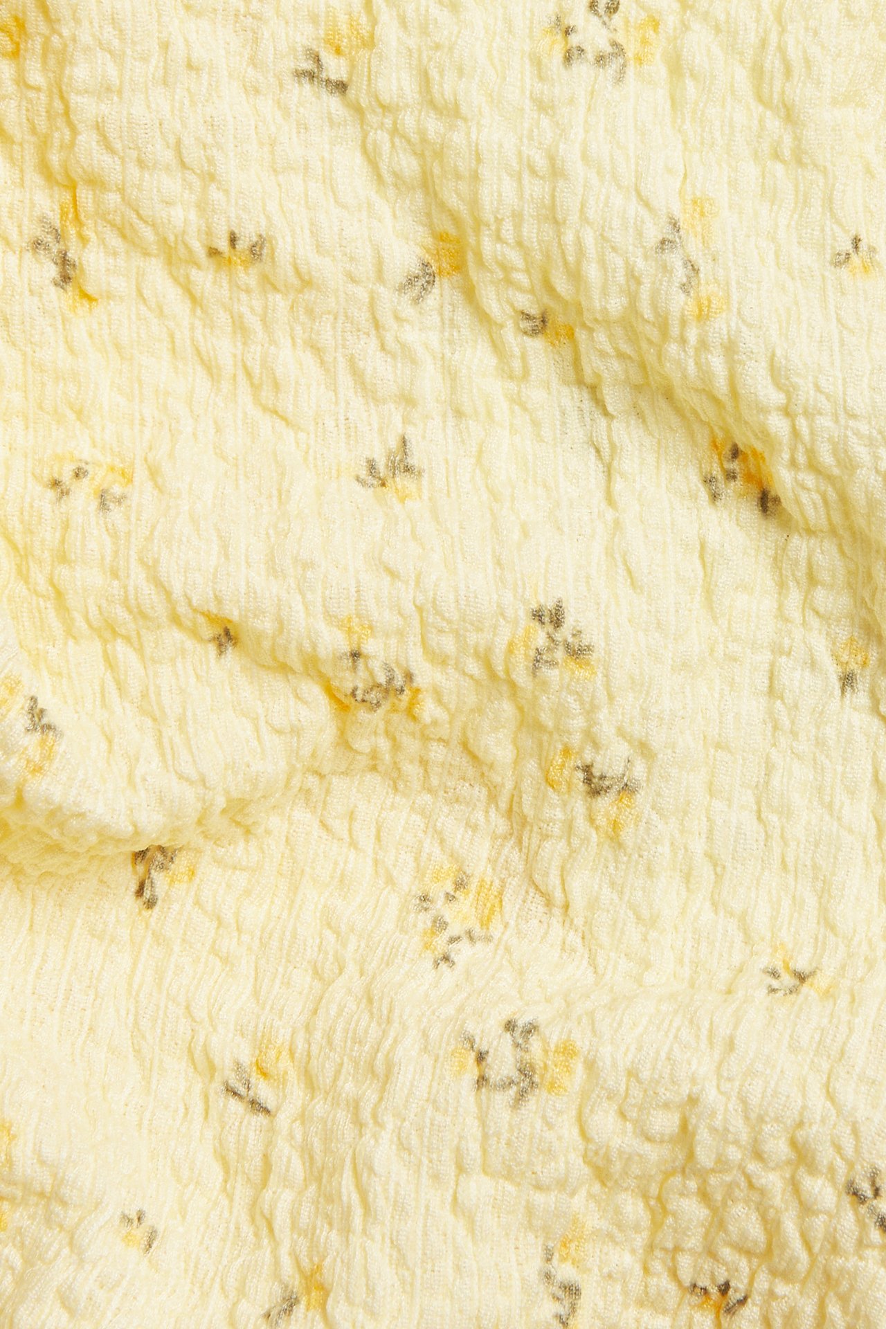 Lähikuva vaaleankeltaisesta kuvioidusta kankaasta, jossa pieni keltainen ja tummanharmaa kukkakuvio.