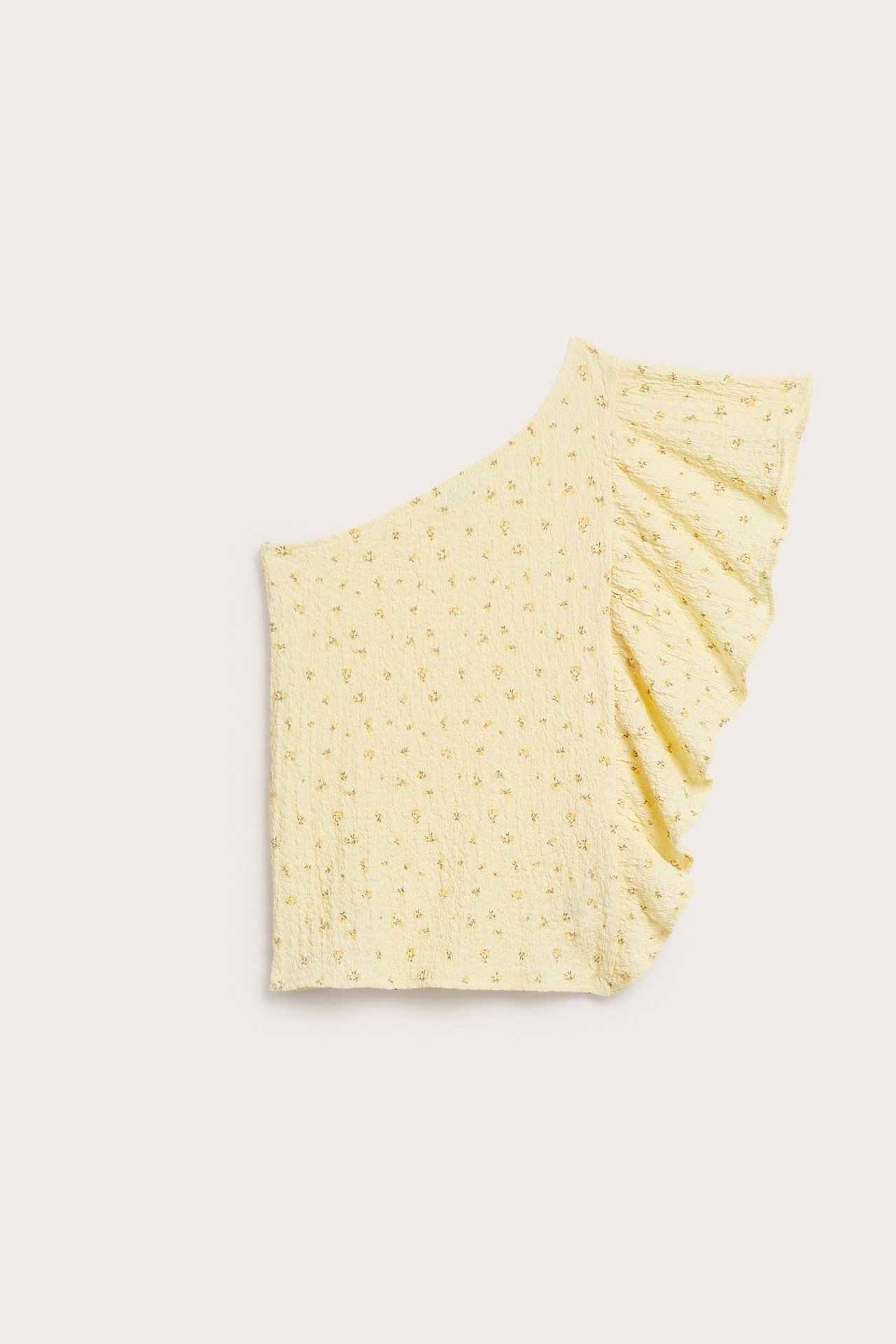 Widok z przodu jasnożółtego topu na jedno ramię z falbanką po boku i drobnym kwiatowym wzorem.