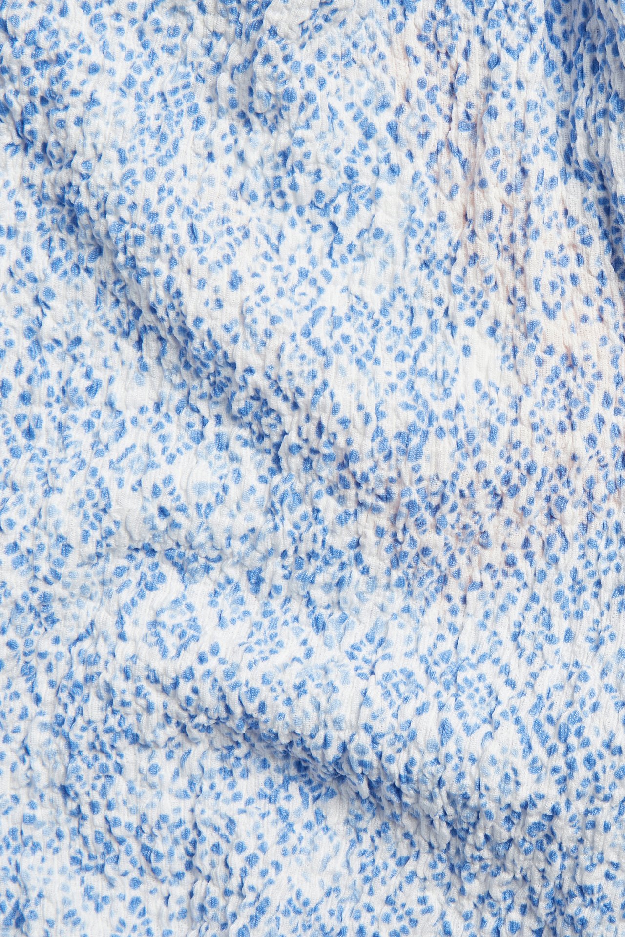 Lähikuva sinivalkoisesta kuviollisesta, poimutetusta kankaasta.