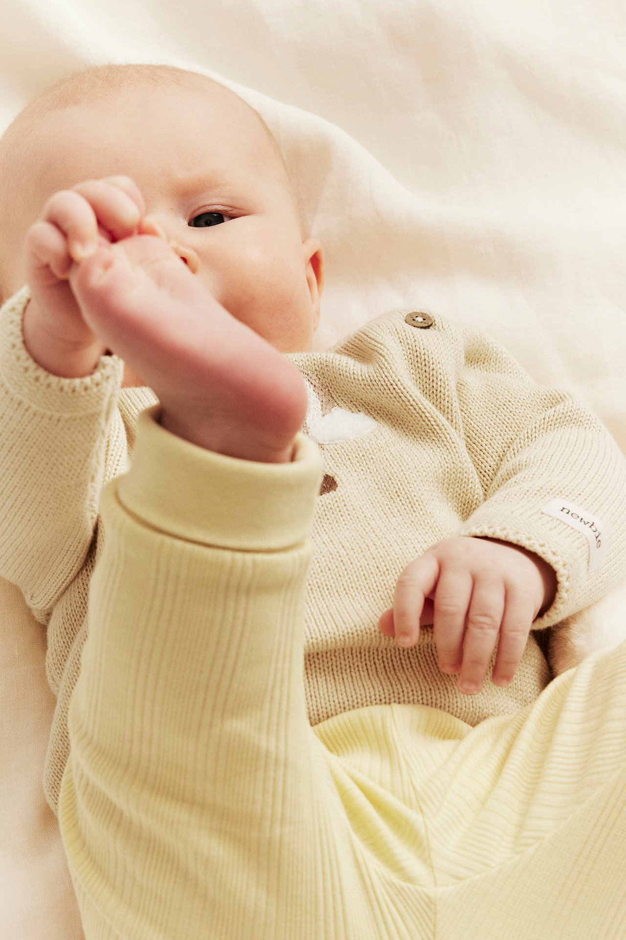 Vauva kermanvärisessä hienoneuleisessa puuvillaneuletakissa, jossa ilmapallokirjonta, ja vaaleankeltaisissa ribbihousuissa.
