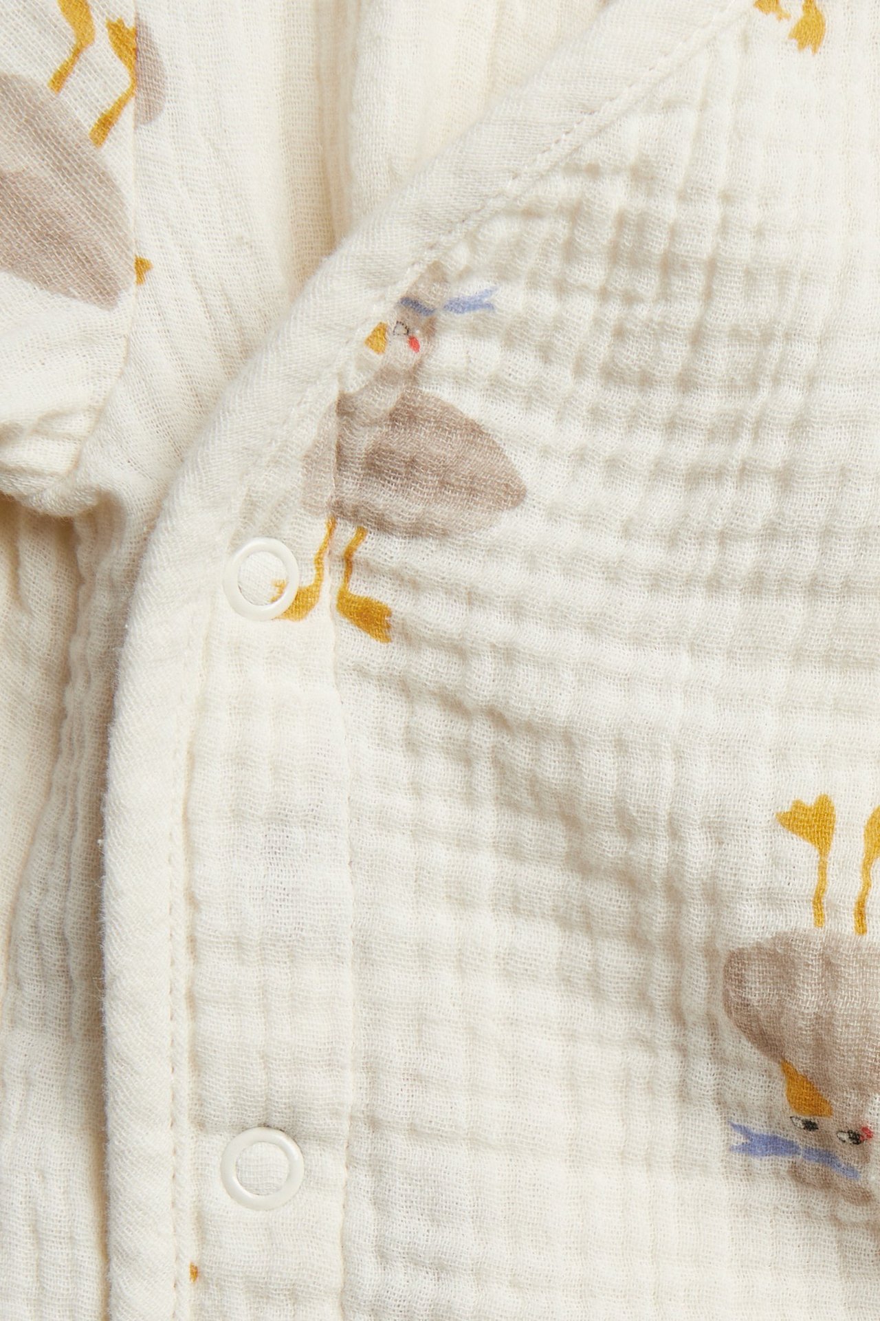 Zbliżenie beżowego body niemowlęcego z muślinu we wzór zwierzęcy z białymi zatrzaskami.