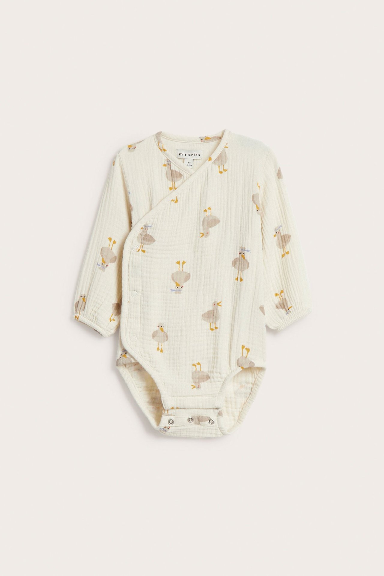 Frontvy av en beige mönstrad omlottbody i muslin med tryckknappar och långa ärmar.