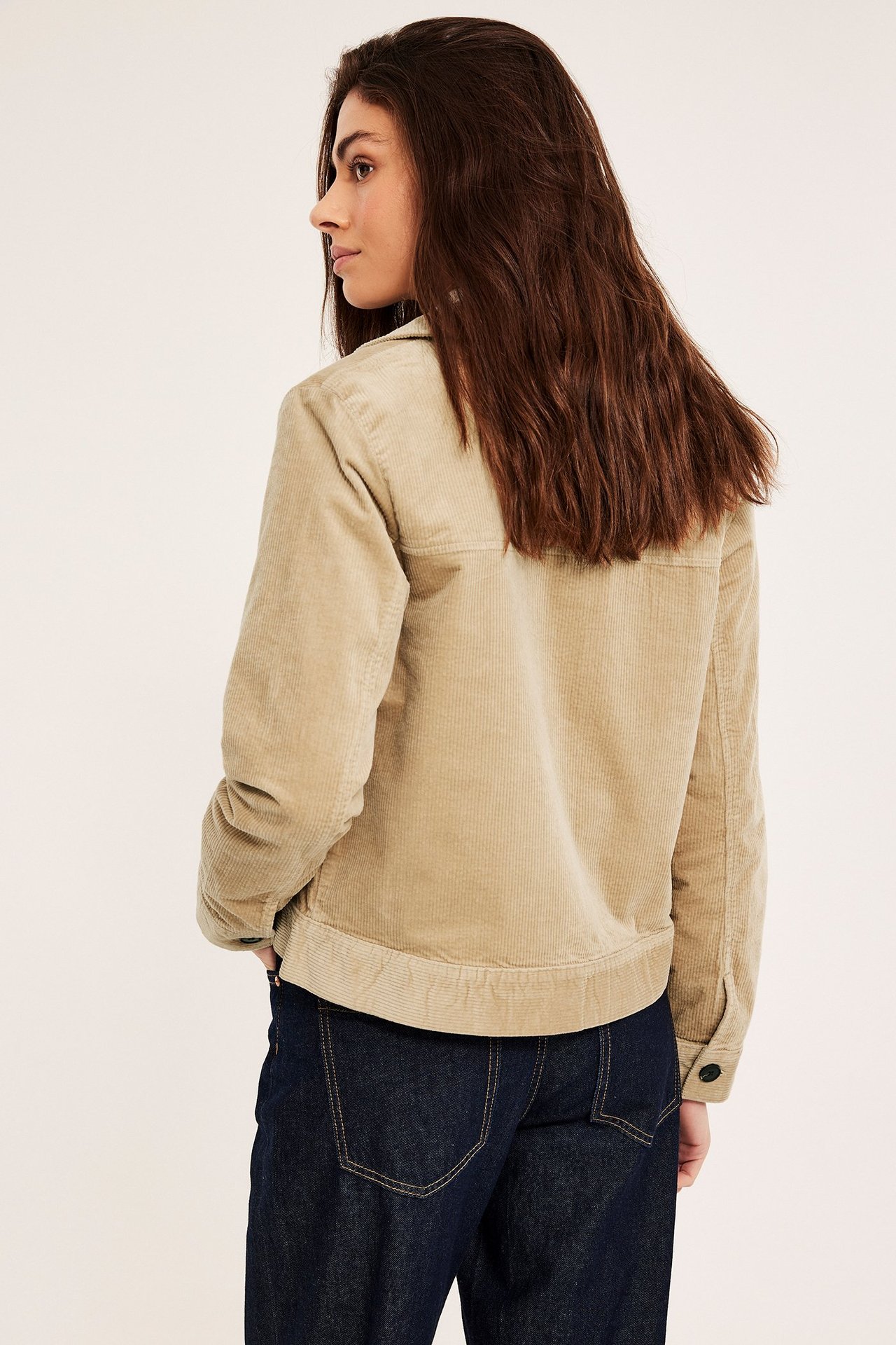 Sidovy bakifrån av en kvinna i en beige kort manchesterjacka med mörkblå jeans.