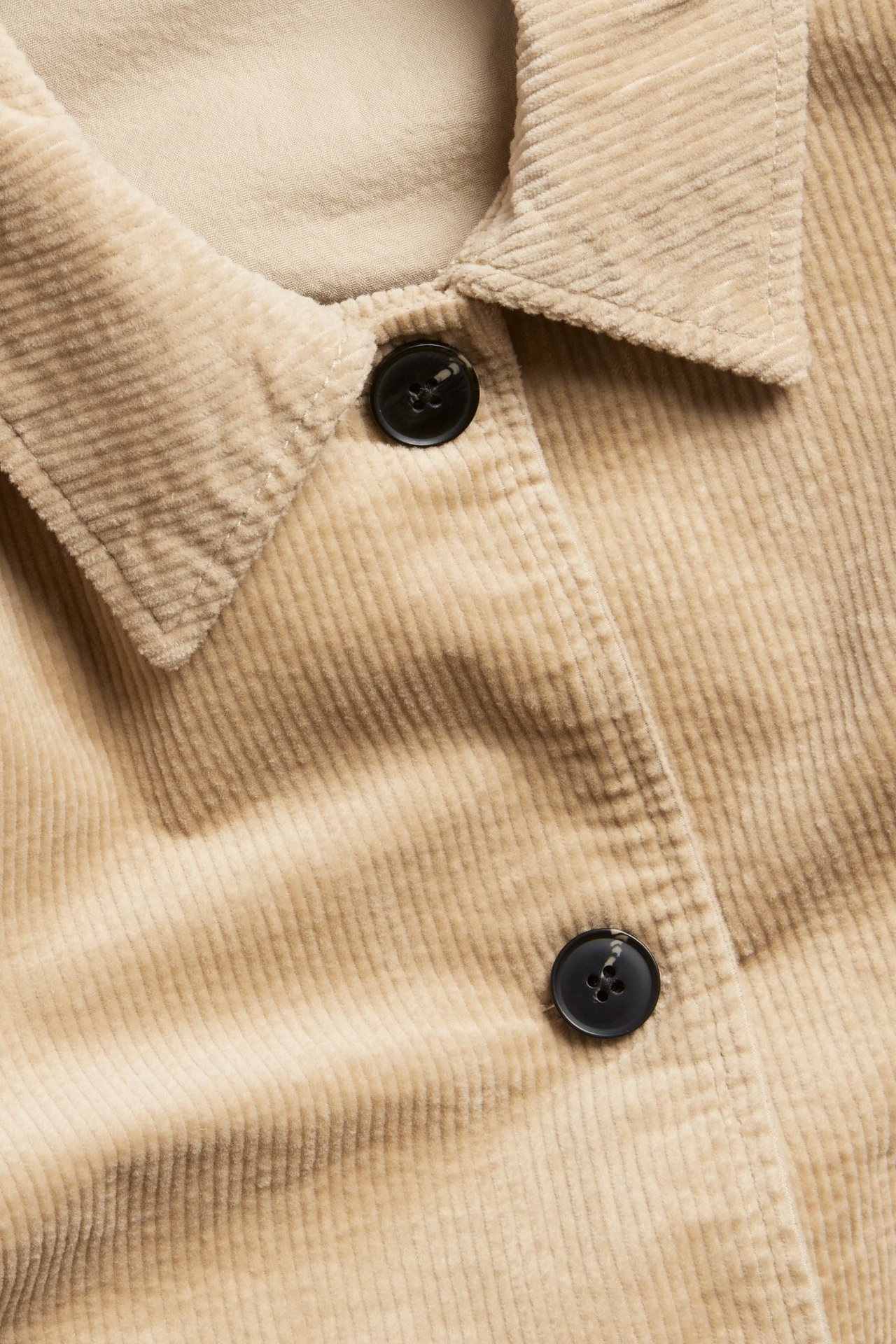 Närbild av en beige manchesterjacka med krage och synliga svarta knappar.