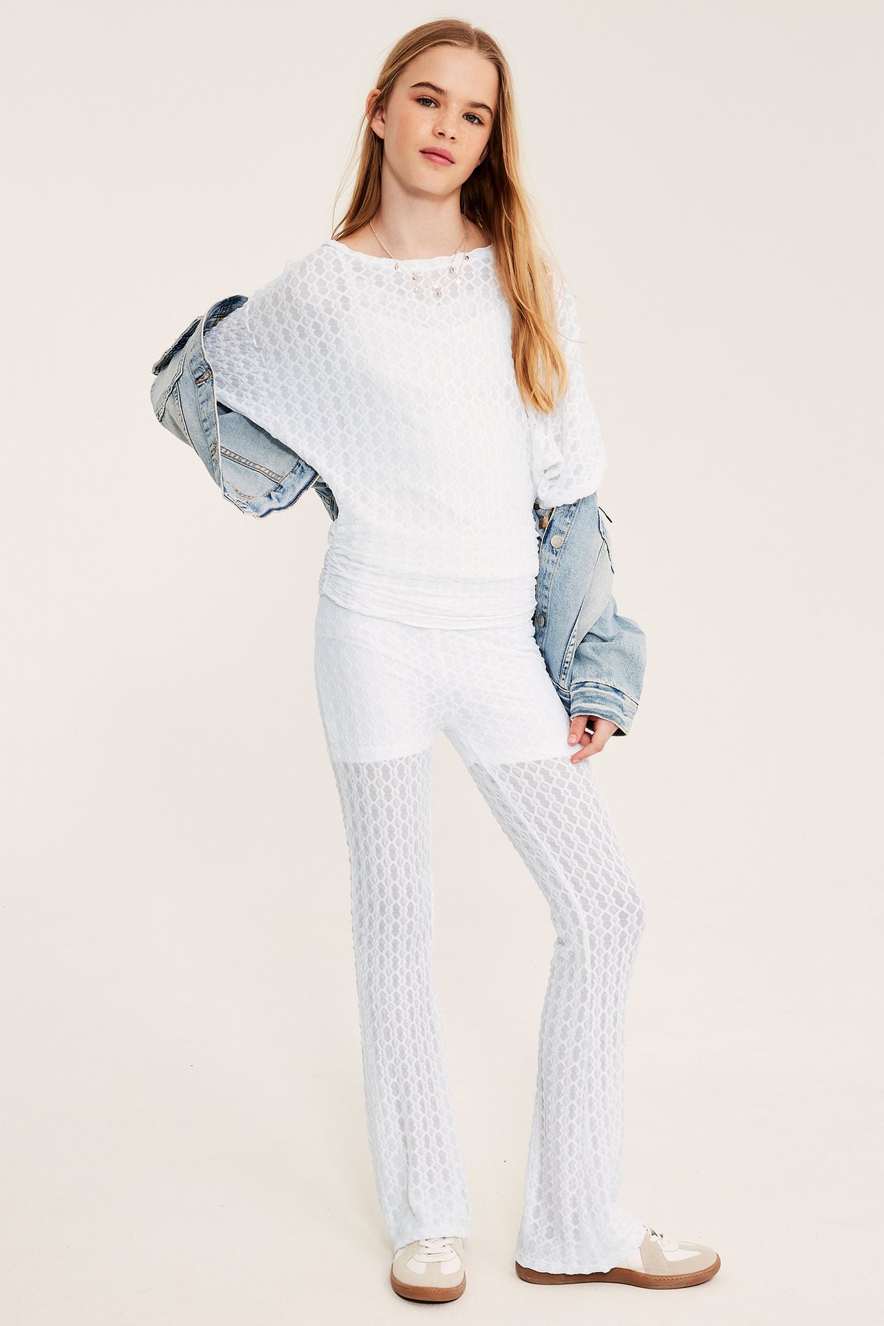 Z przodu: dziecko w białym koronkowym topie z dekoltem łódkowym, marszczoną talią, pasującymi dzwonami i kurtką jeansową.