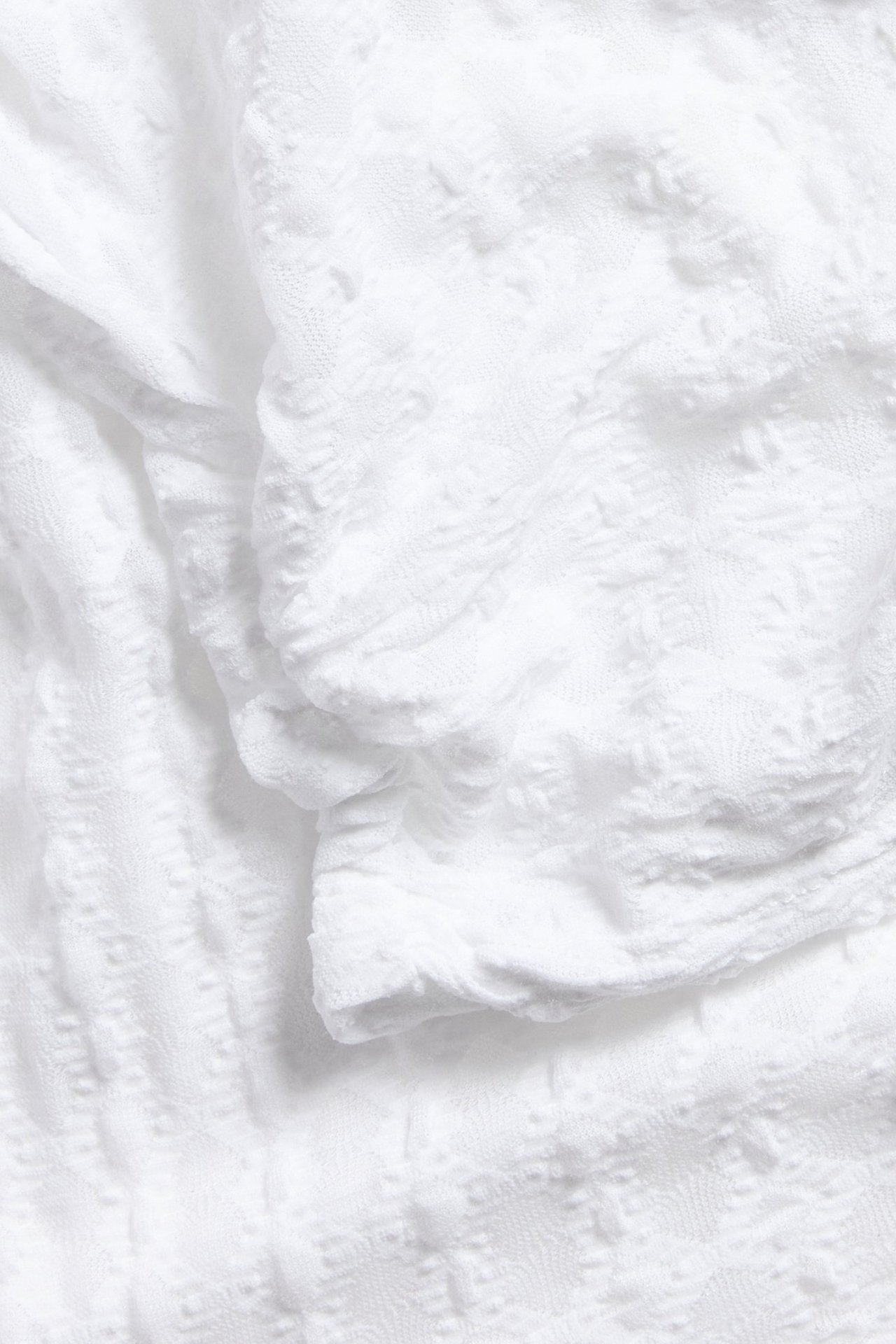 Närbild av en vit spetstopp med rynkade detaljer, som framhäver det texturerade mönstret.