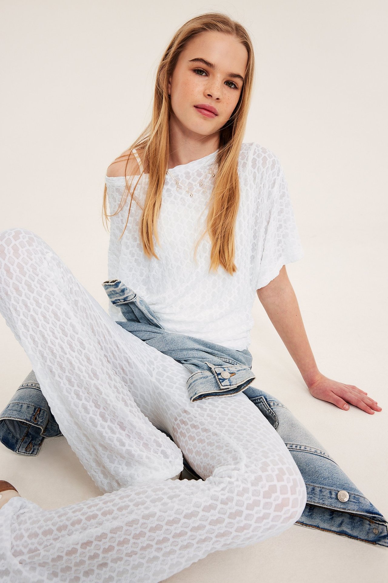 Hvitt topp med sommerfuglslermer, tettsittende midje, blonde mønster, kvinne i blå jeans.