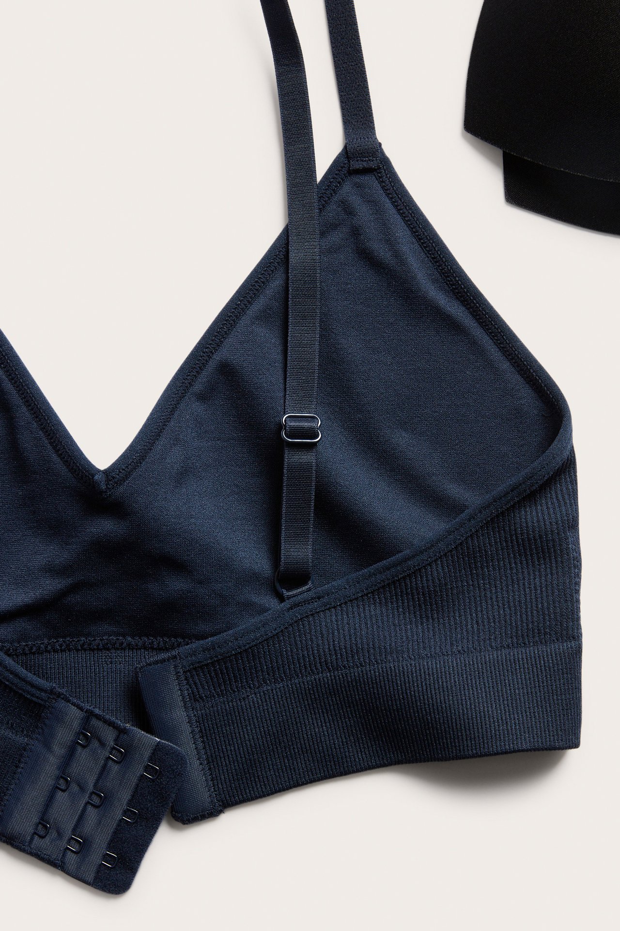 Närbild av en mörkblå ribbad seamless bh med justerbara band och hak- och hyskknäppning. Del av svart bh synlig.
