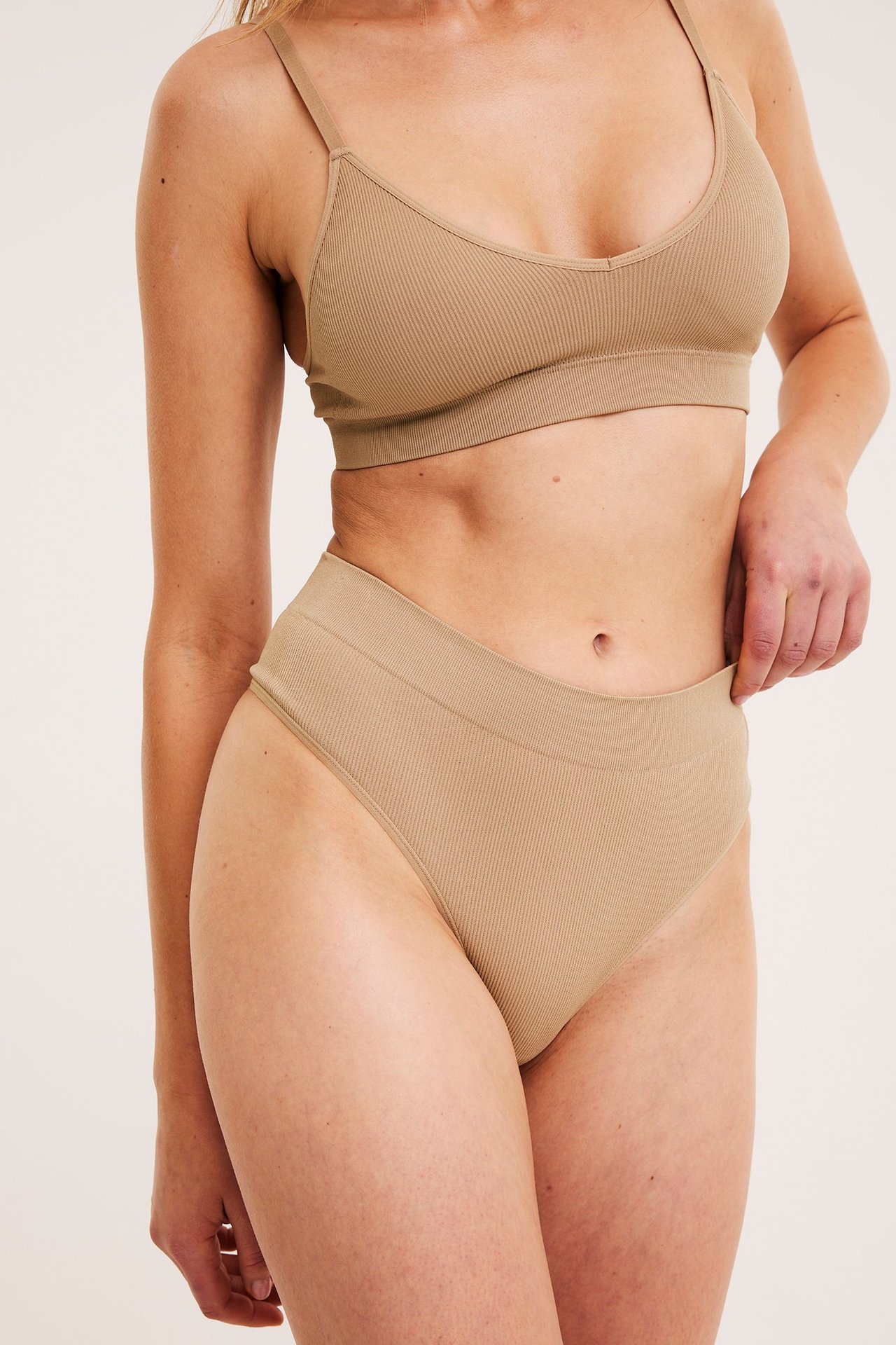 Närbild framifrån av en kvinna i brun ribbad sömlös stringtrosa och matchande bralette.