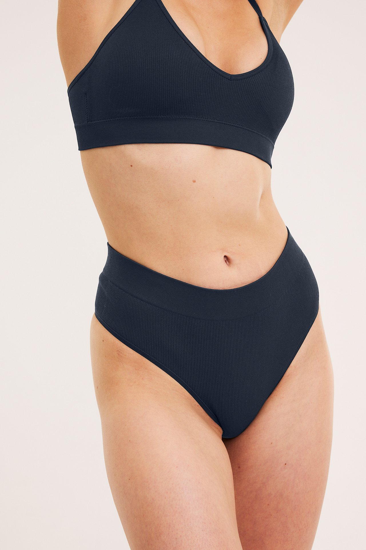 Forfra: kvinne i mørkeblå ribbet sømløs stringtruse og matchende bralette.