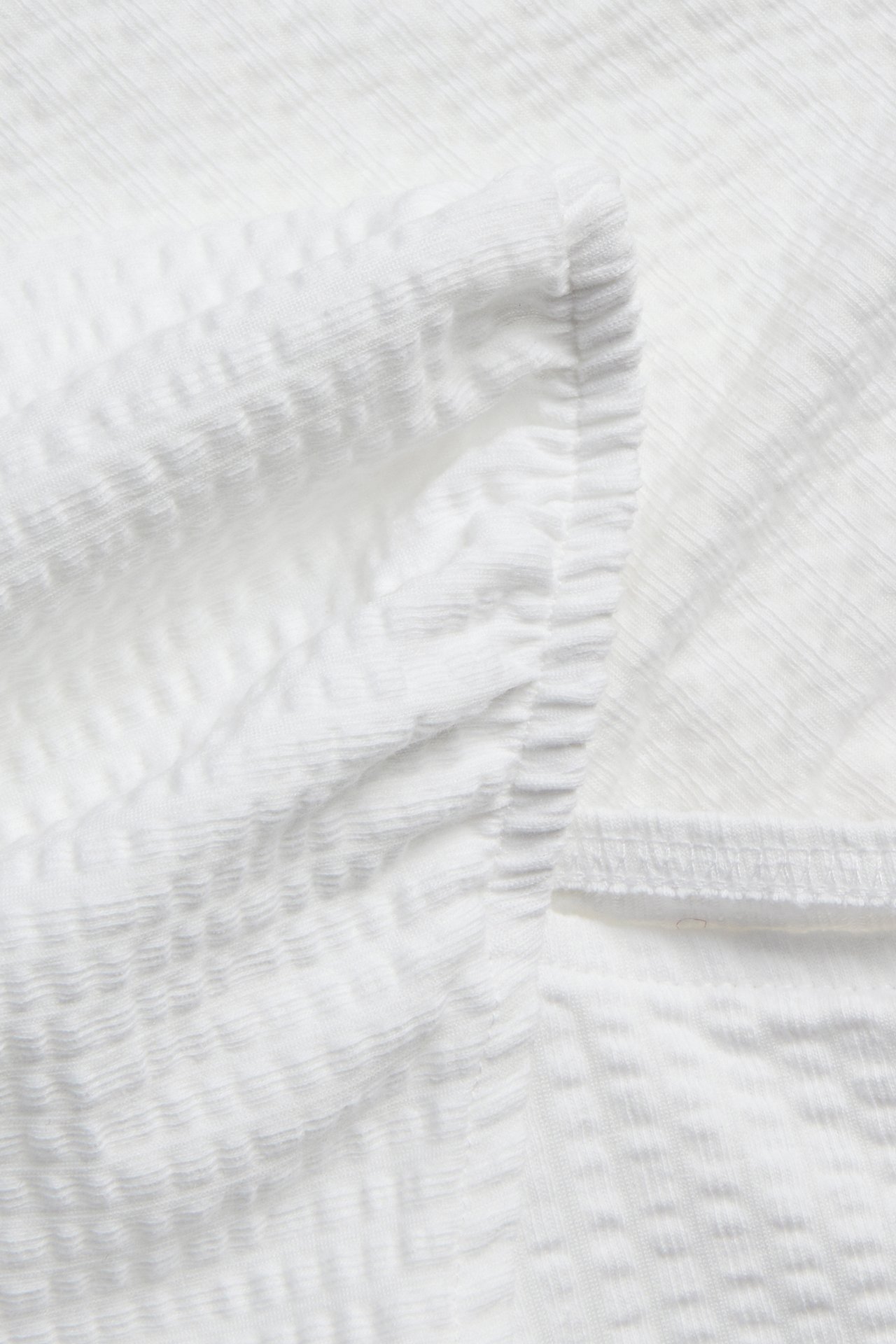 Zbliżenie białego, teksturowanego, marszczonego topu, przedstawiające detal tkaniny i marszczony szew.