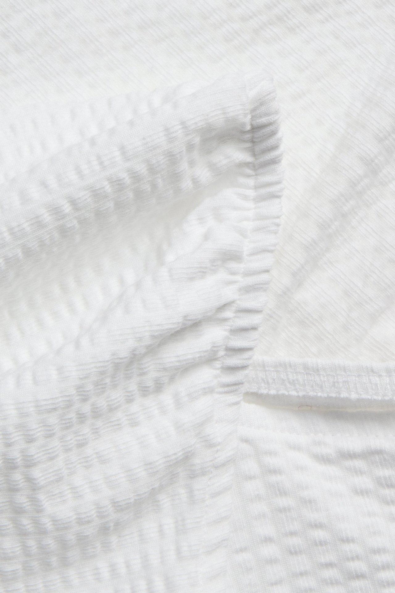 Zbliżenie białego, teksturowanego, marszczonego topu, przedstawiające detal tkaniny i marszczony szew.
