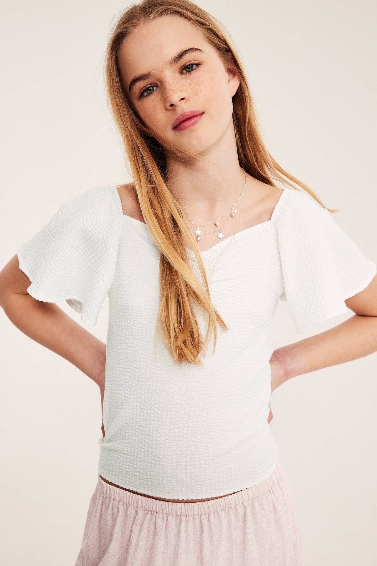 Valkoinen tiukka toppi röyhelöillä ja perhossivuilla, nuoren naisen päällä.