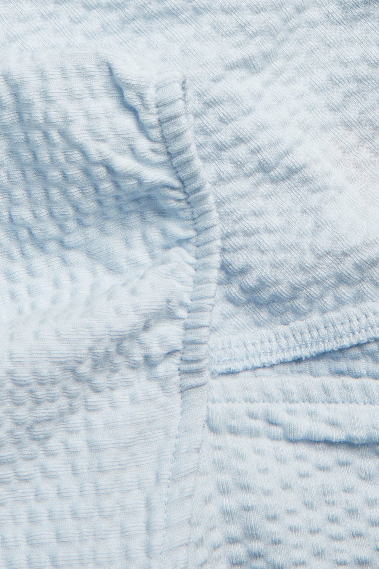 Zbliżenie na jasnoniebieski top z marszczonym przodem i teksturowanym, pofałdowanym materiałem.