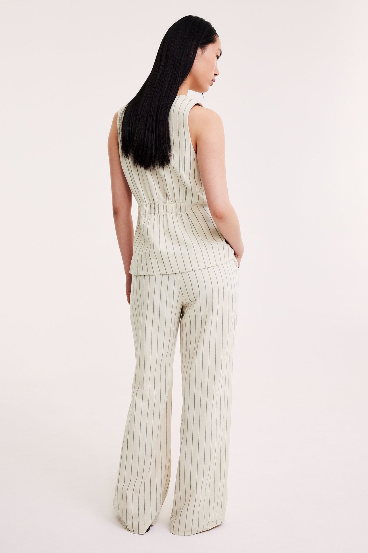 Widok z tyłu: kobieta w kremowych szerokich spodniach w paski i pasującej kamizelce.