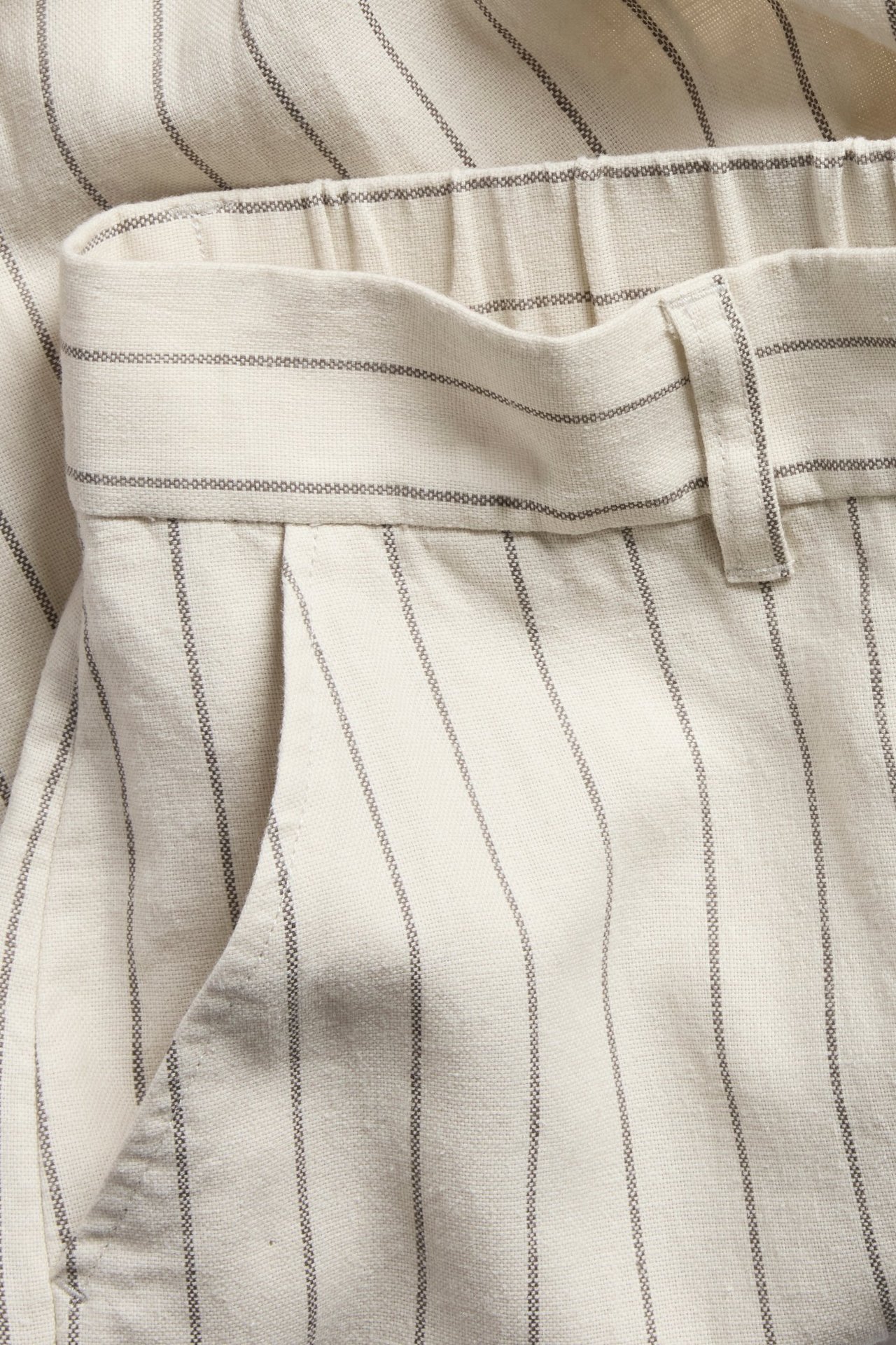 Zbliżenie na białe, prążkowane spodnie garniturowe z elastycznym pasem i przednią kieszenią.