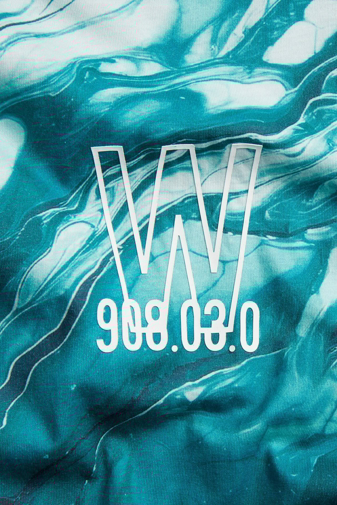 Zbliżenie: Dziecięcy T-shirt oversize z off-white bawełny, turkusowym marmurowym wzorem i białym nadrukiem.