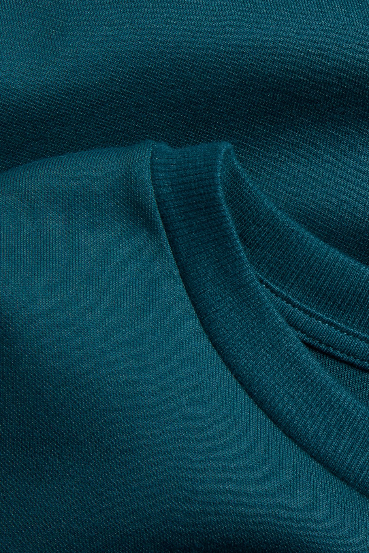 Lähikuva vihreästä ylisuuresta t-paidasta, näyttää kankaan tekstuurin ja resori pääntien.