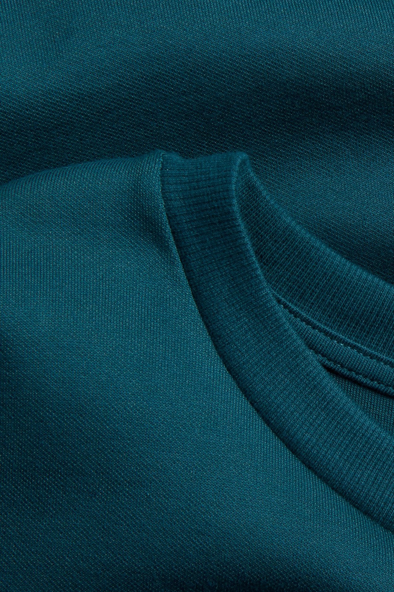 Zbliżenie zielonego, obszernego T-shirtu, ukazujące fakturę materiału i prążkowany dekolt.