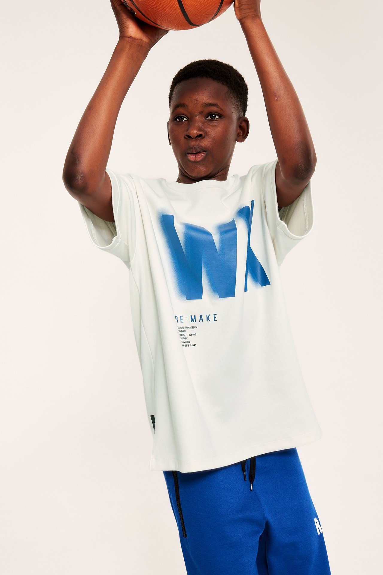 Frontbilde: Barn i hvit oversized t-skjorte med blått trykk, blå bukser, holder en basketball.