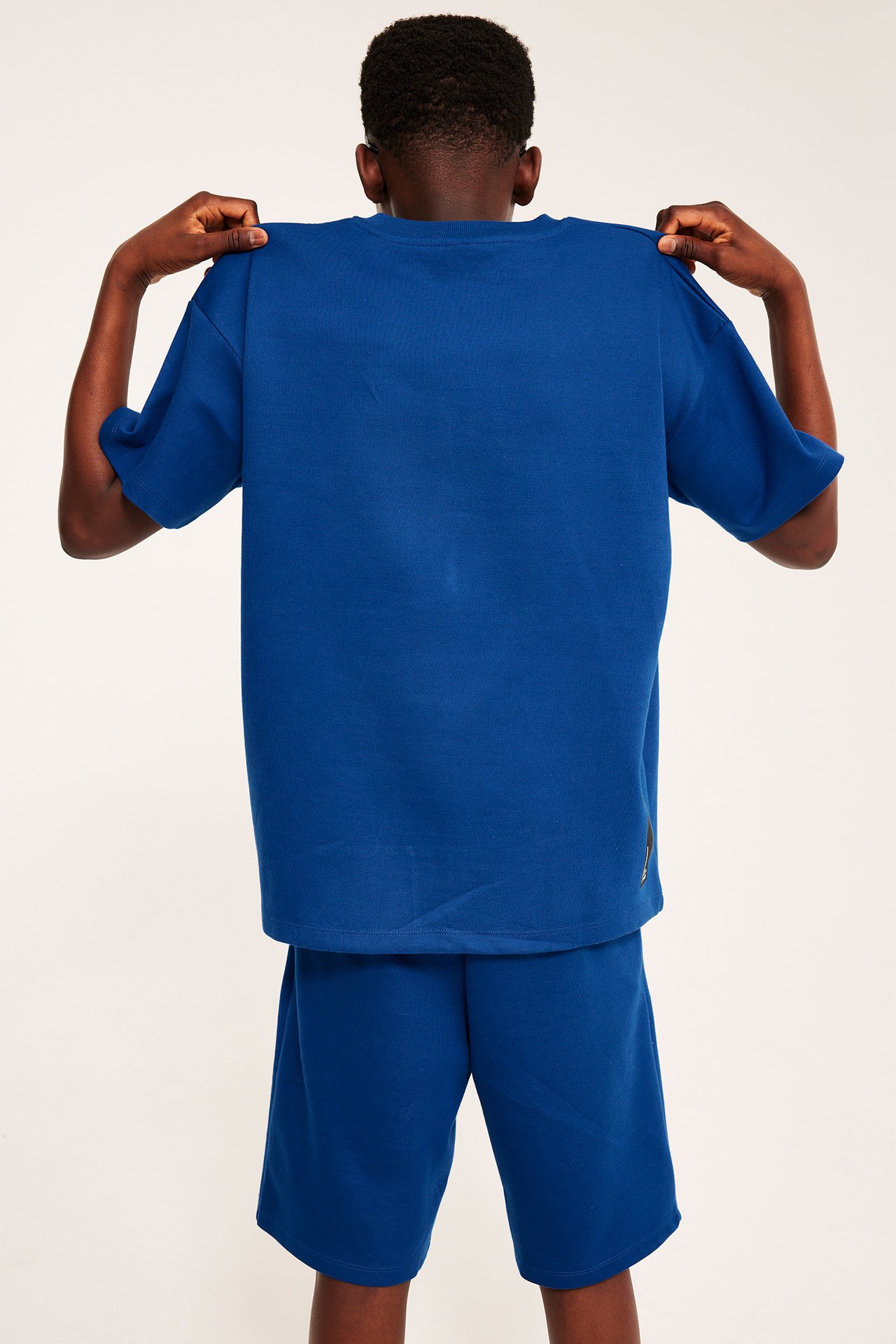 Bakfra: et barn drar opp en mørkeblå oversized T-skjorte med matchende shorts.