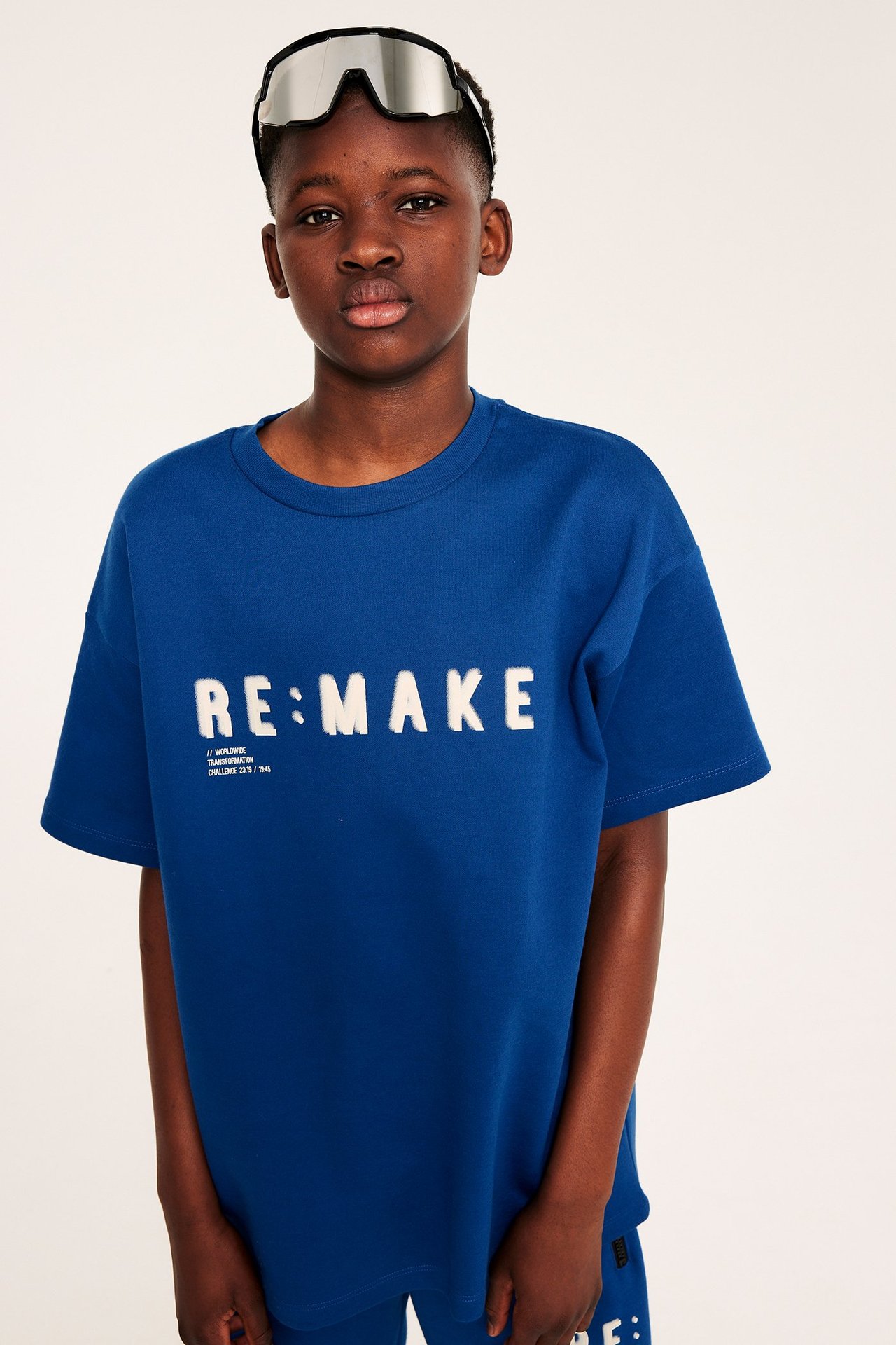 Framsida: Barn i mörkblå oversized t-shirt med 'RE:MAKE' tryck och spegelglasögon.