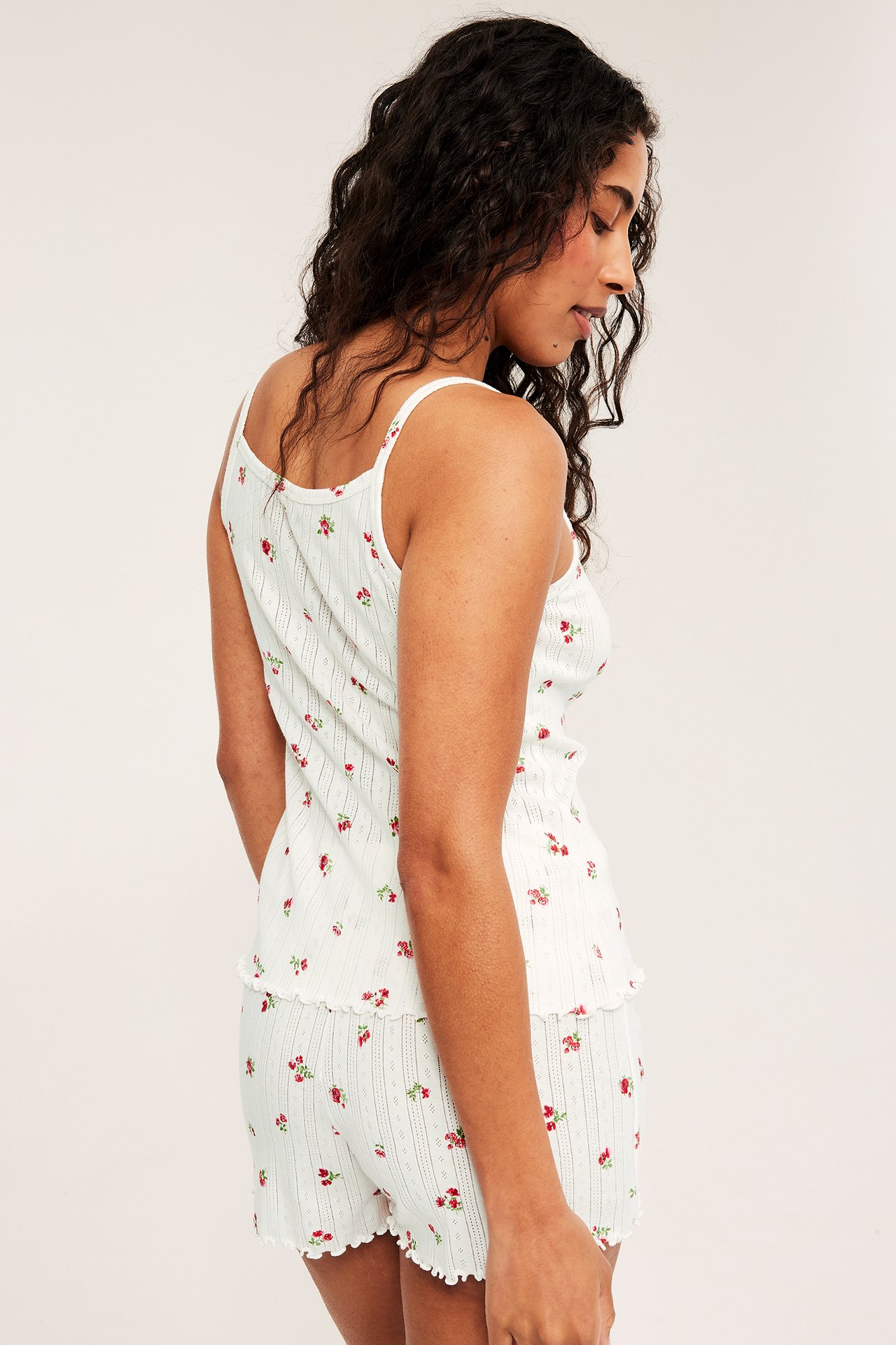 Sideprofil av kvinne i hvitt bomulls-pointelle pyjamasett med rødt blomstermønster og volangkant.