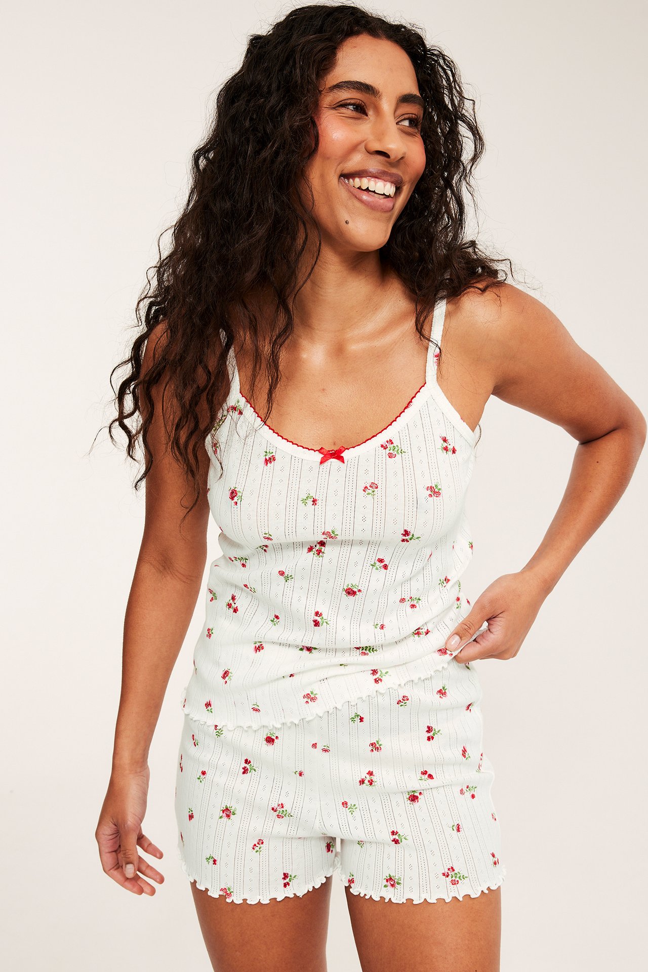 Forfra, kvinne i et hvitt pyjamasett i bomullspointelle med rødt blomstermønster.