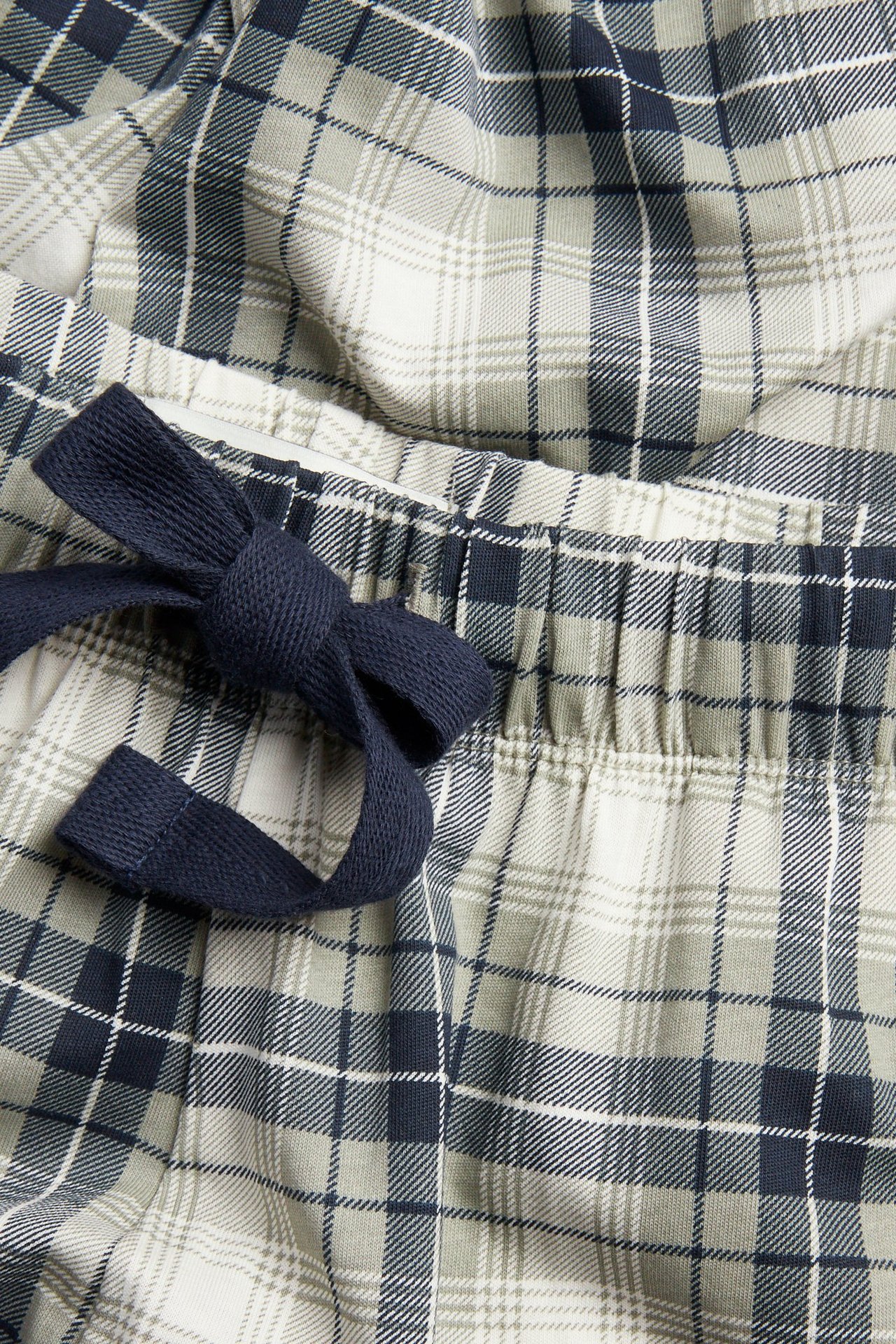 Närbild: pyjamasbyxor i bomull för herr, rutiga i ljusgrönt, vitt, mörkblått, med mörkblå dragsko.