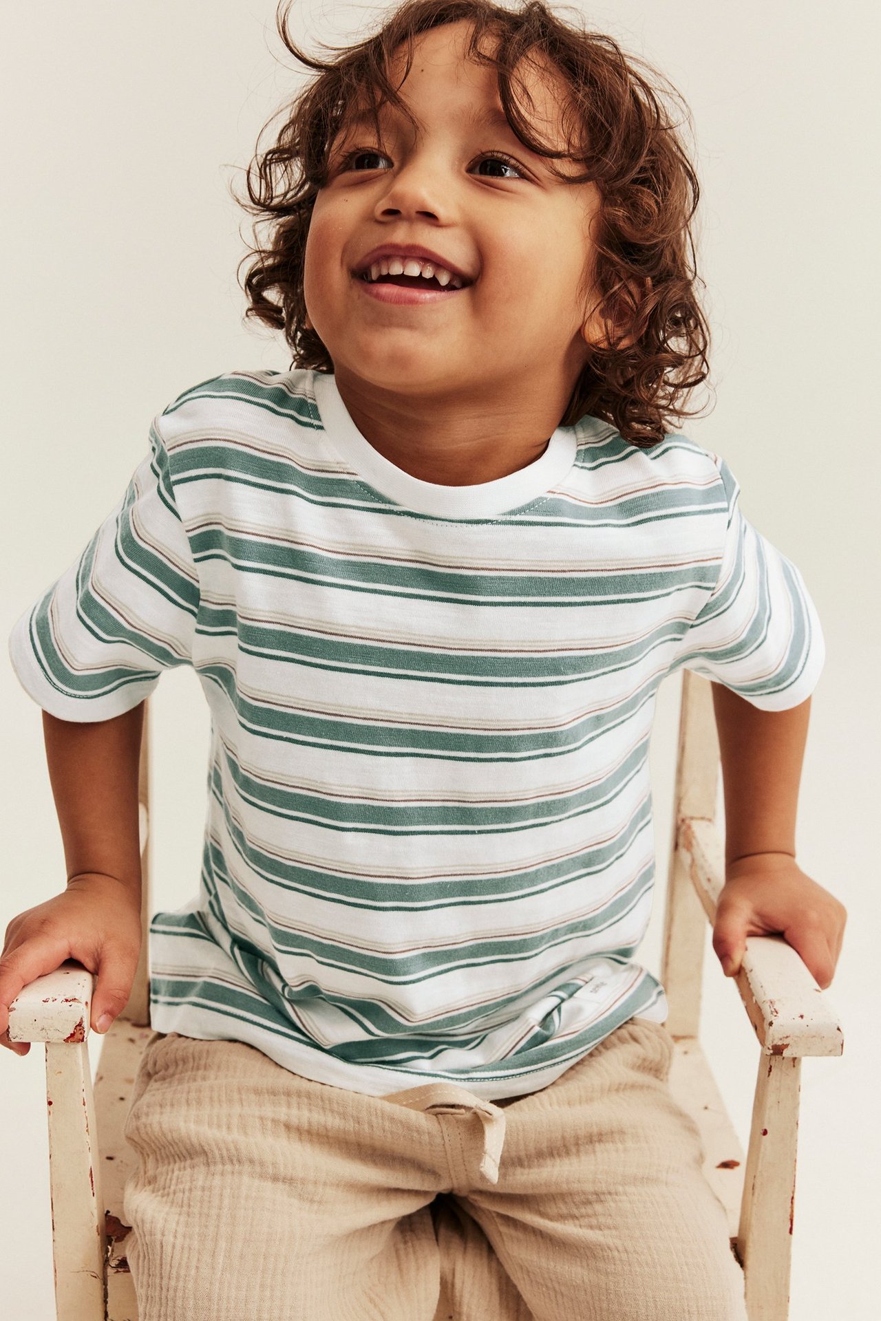 Framifrån: Barn i offwhite och grönrandig t-shirt med uppvikta ärmar och beige byxor.