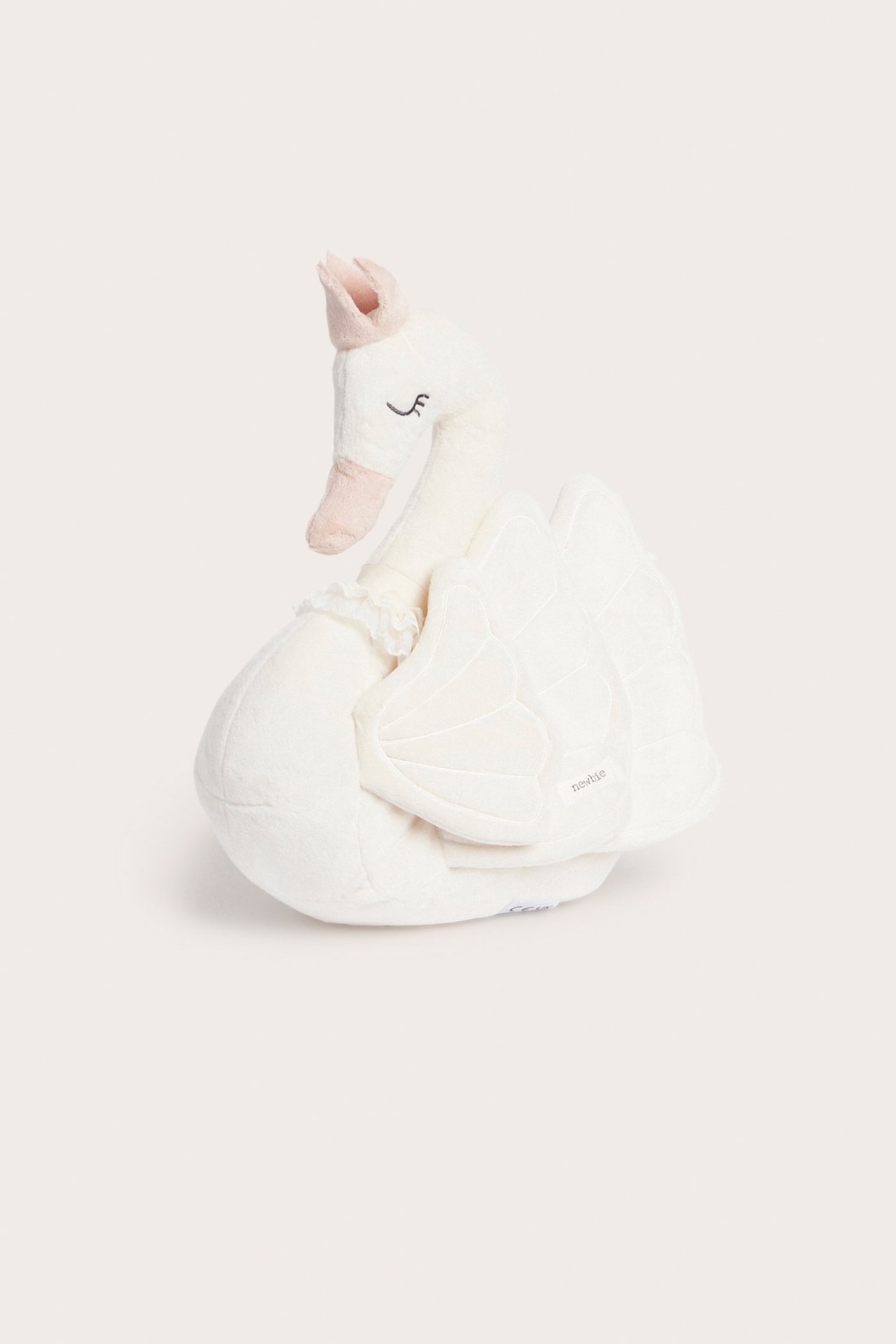 Widok z przodu na kremową, miękką poduszkę w kształcie łabędzia z różową koroną.