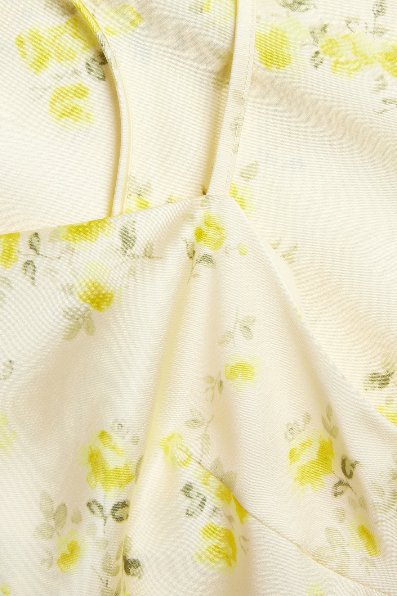 Nærbilde av en lysegul asymmetrisk slipkjole med gult blomsterjacquardmønster og tynne stropper.